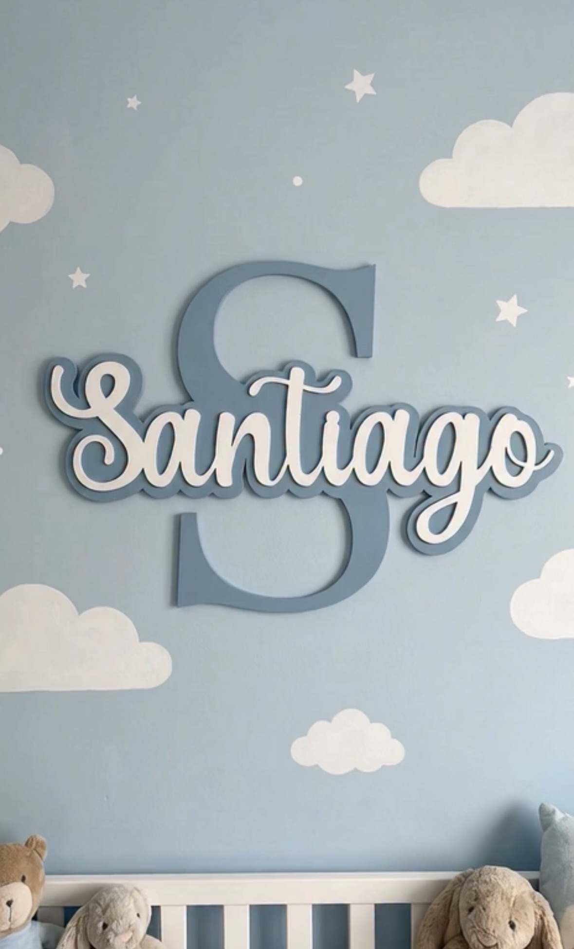 Decorative wall with large letter 'S', name 'Santiago', clouds, stars, and a teddy bear on a bed.