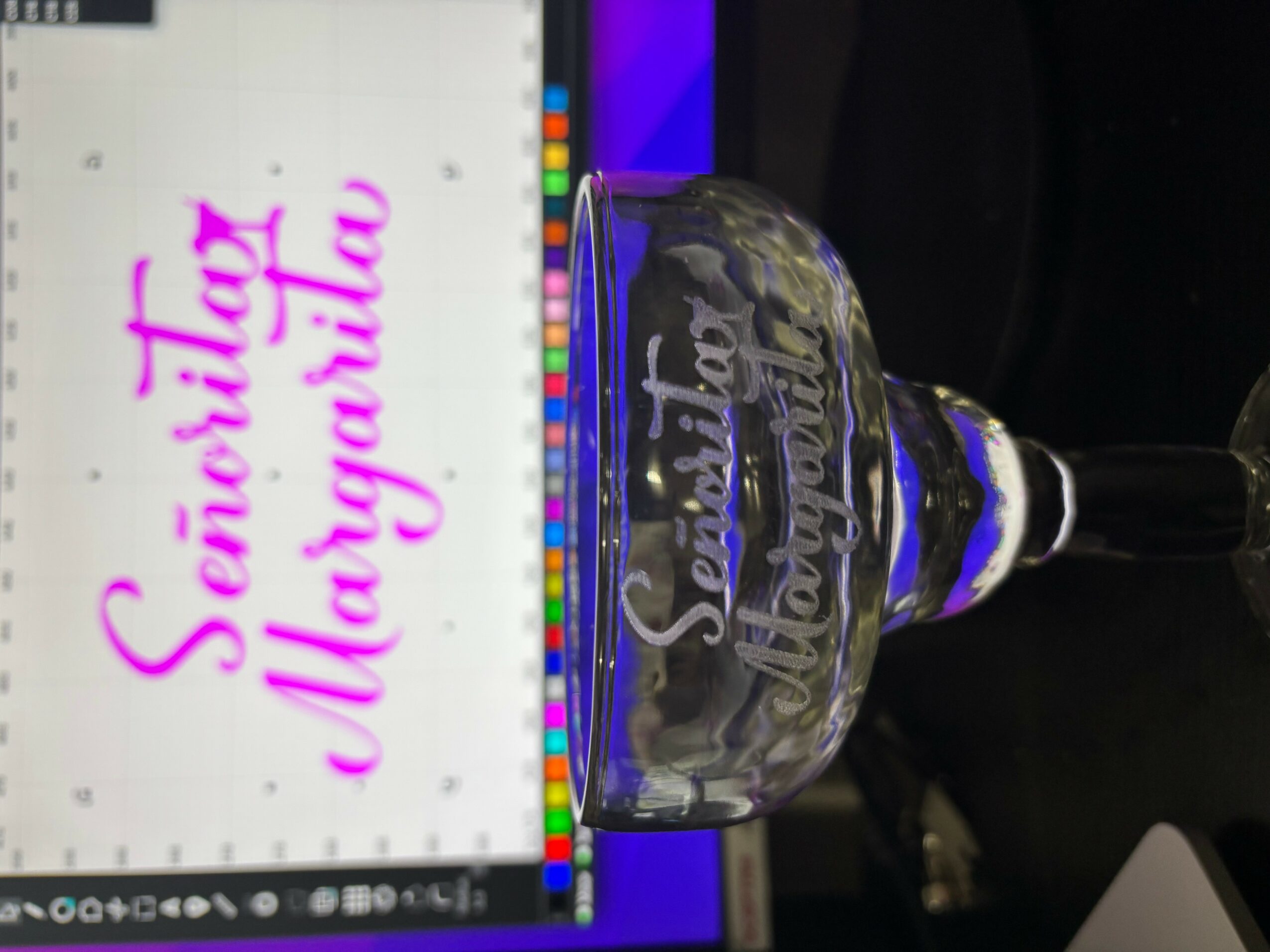 Glass with text 'Scented Margarita' in front of a computer screen displaying similar text, on a dark surface.
