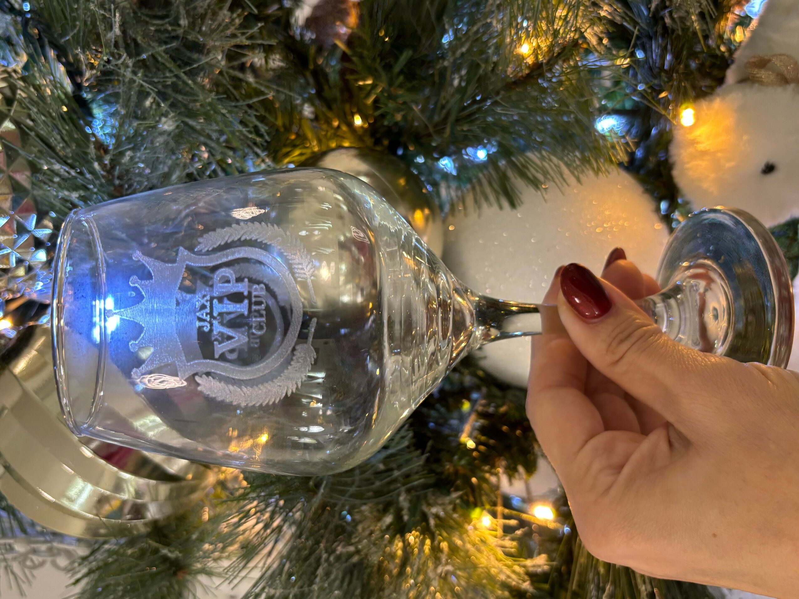 Person holding a wine glass in front of a decorated Christmas tree with lights and ornaments.