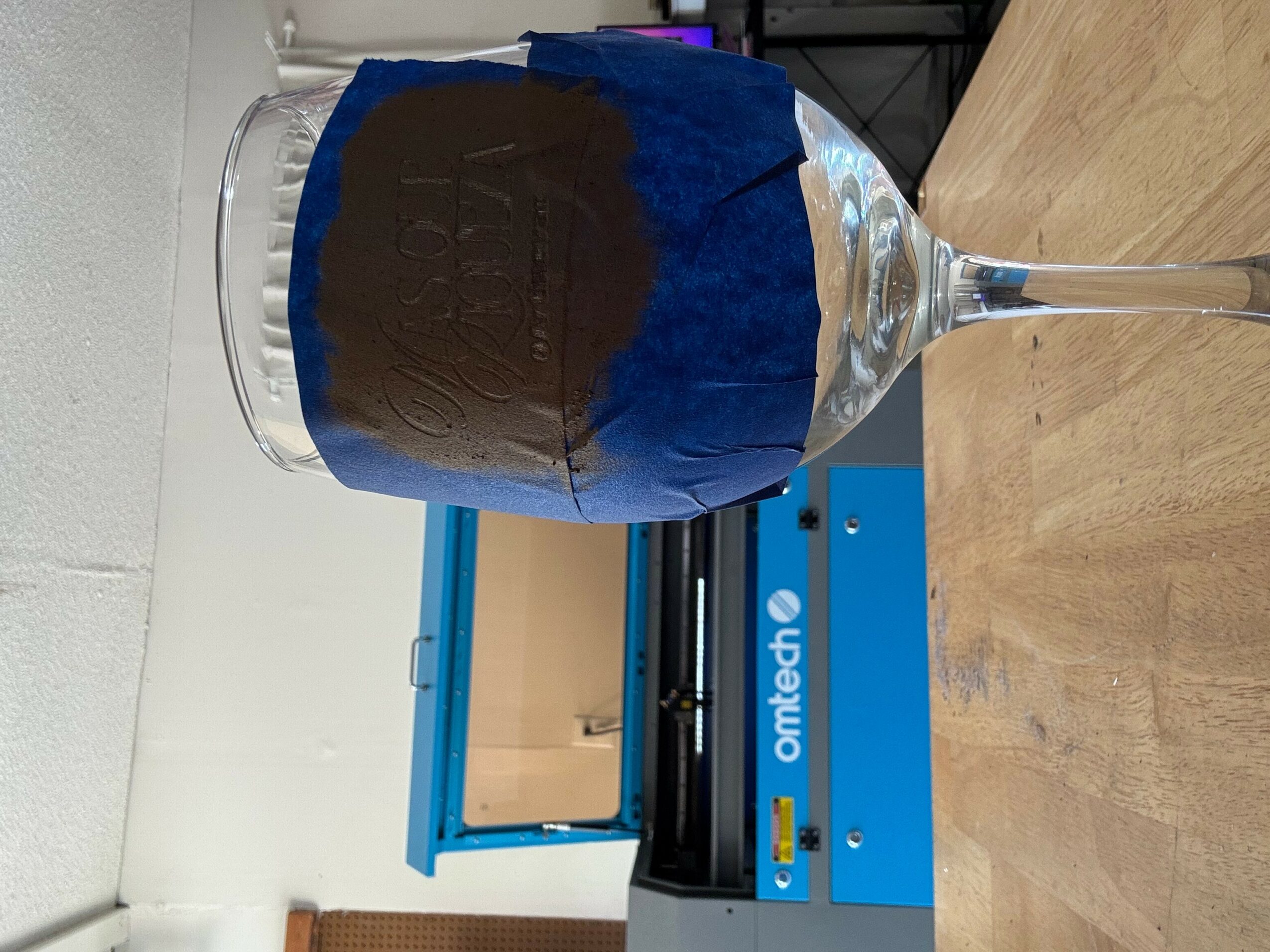 A glass with a dark liquid and a blue napkin, placed on a wooden surface, with a blue device in the background.