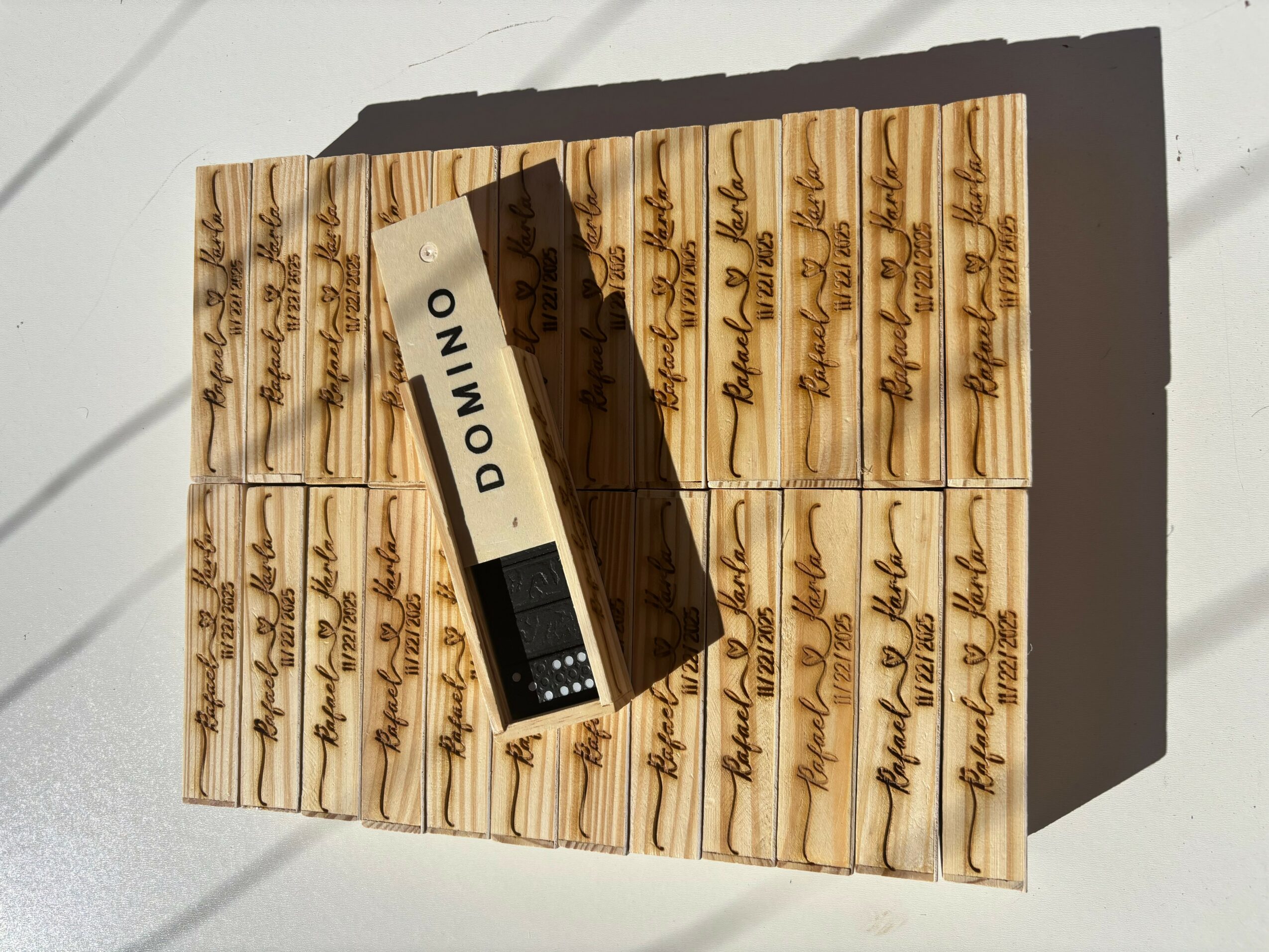 A box of domino tiles with handwritten labels, and a small black and white device on top, casting a shadow.