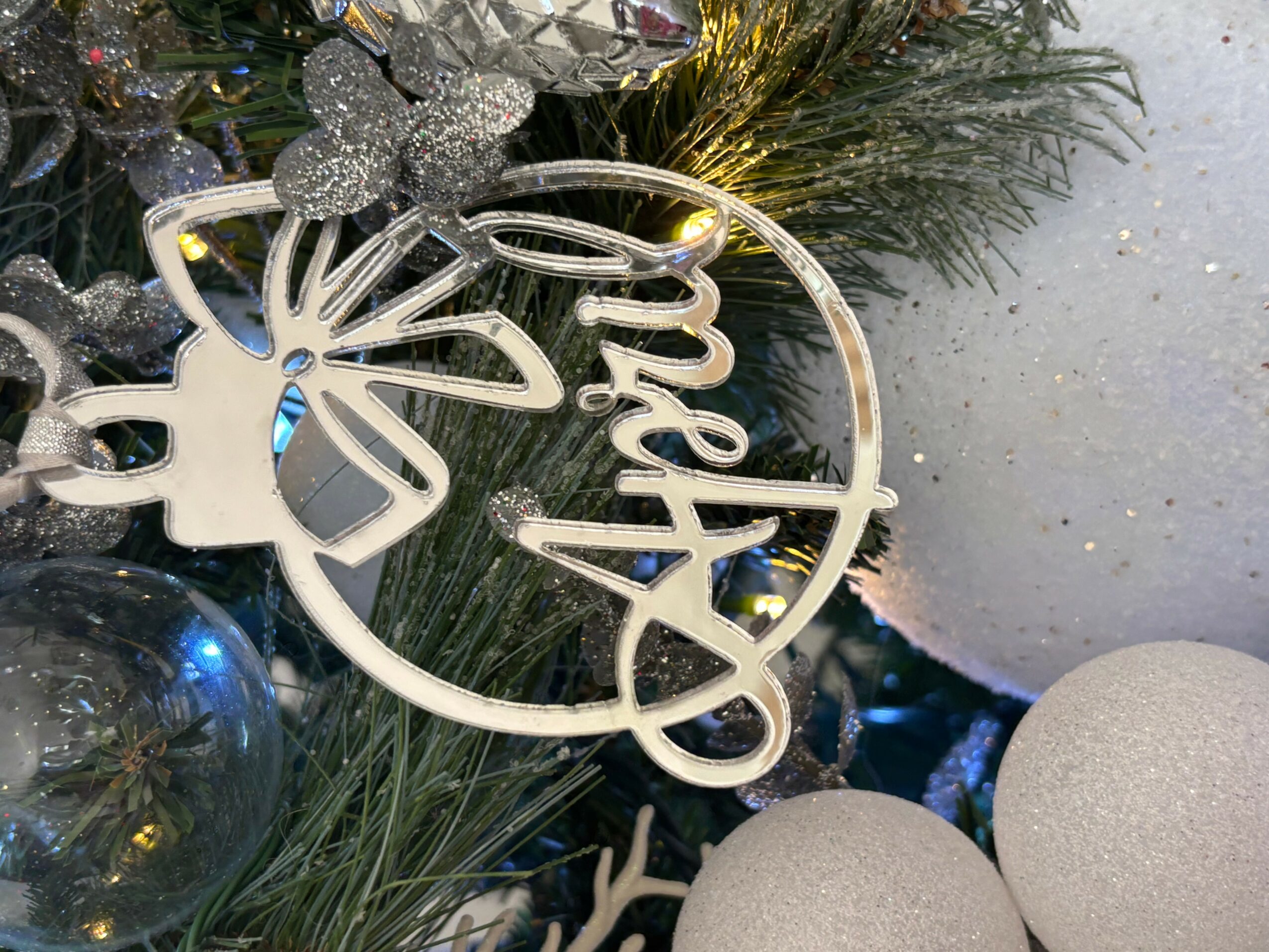 Christmas ornament with the word 'Merry' hanging on a decorated tree branch, surrounded by ornaments and greenery.