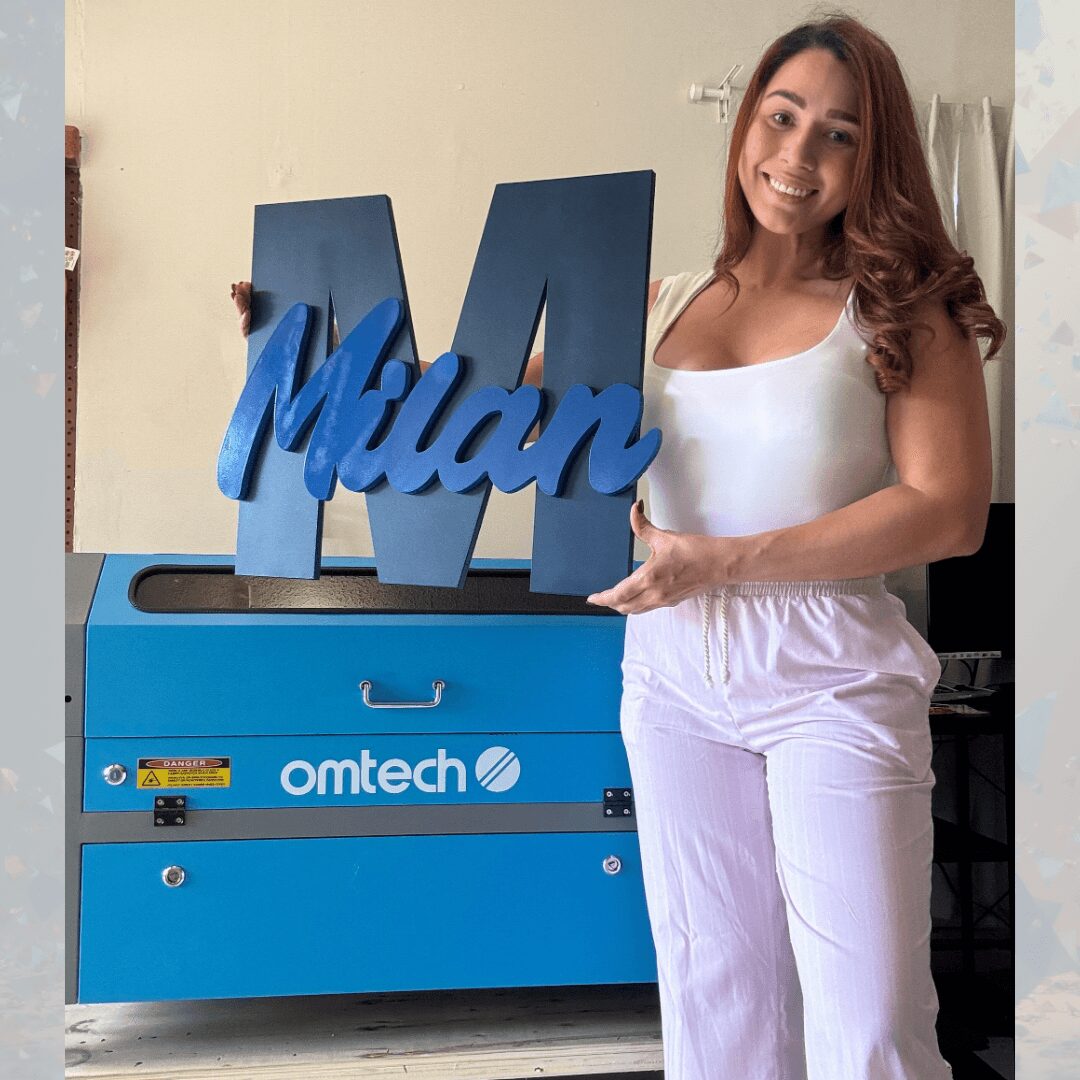 Woman standing next to a blue machine with a large 'M' and the name 'Milan' on it, smiling, in a room.