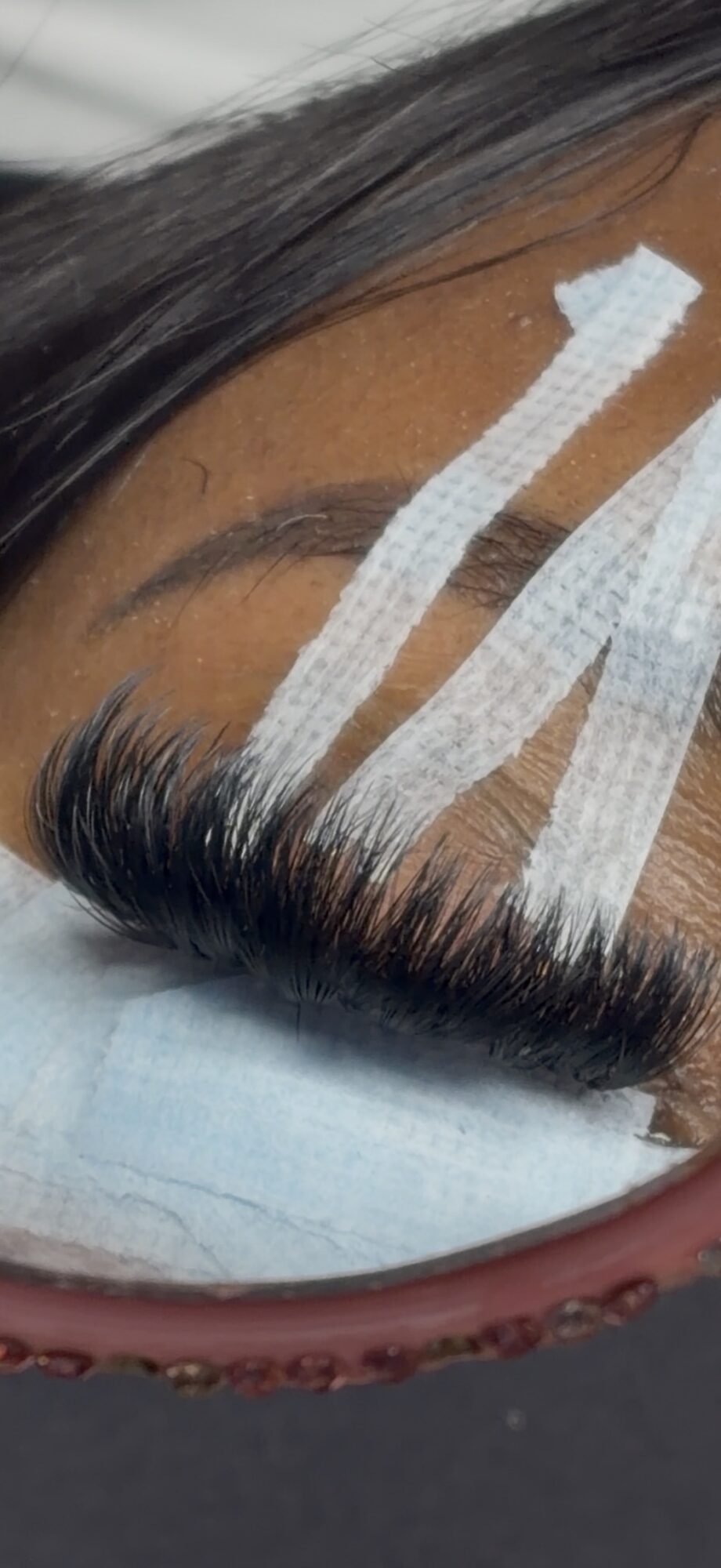 Close-up of a person's forehead with eyelash extensions and medical tape, eye closed, skin visible.