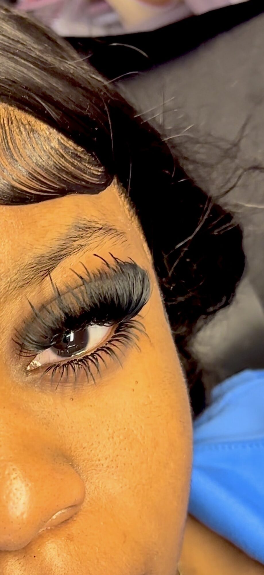 Close-up of a person's eye with long eyelashes, partially visible face, and dark hair, lying on a surface.