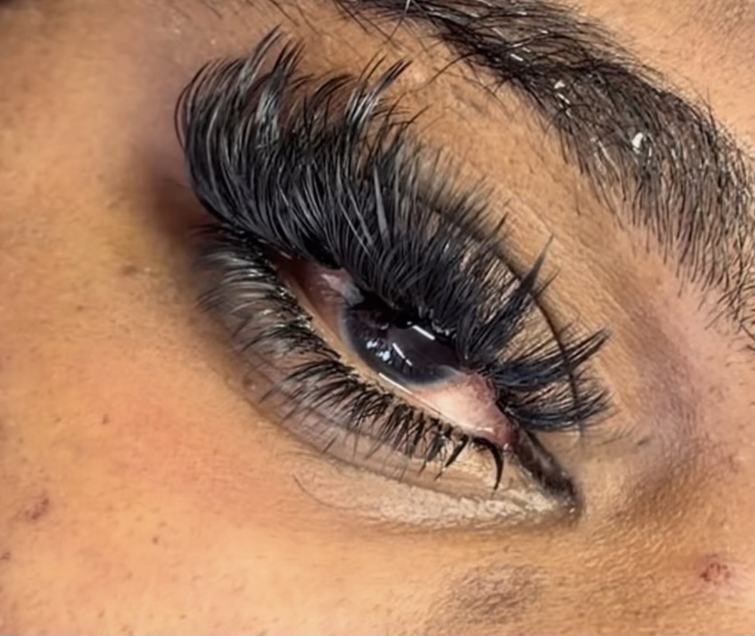 Close-up of a person's eye with long, thick eyelashes and well-defined eyebrow, eye makeup, and visible skin texture.