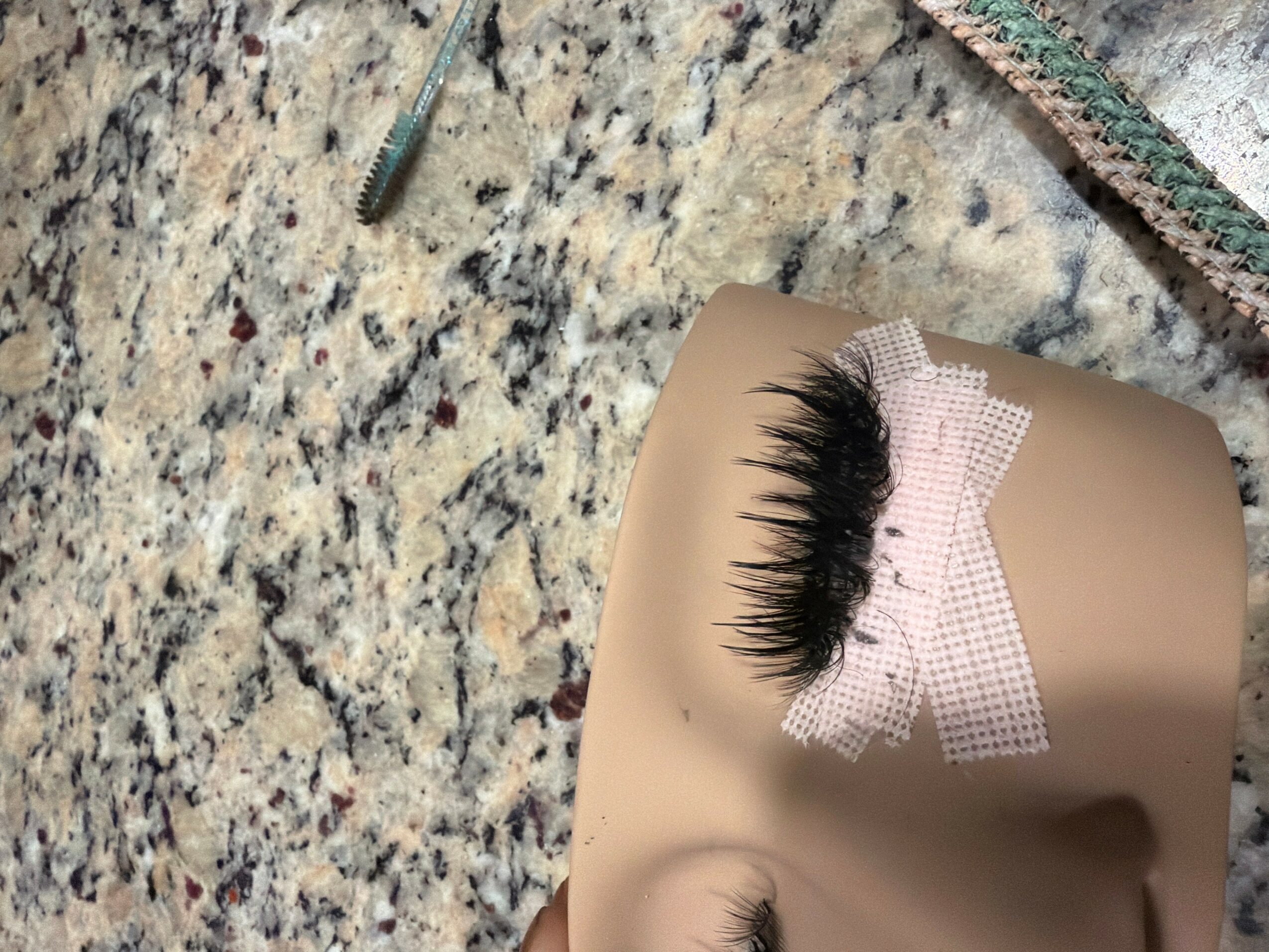 False eyelashes taped to a beige surface on a speckled countertop.