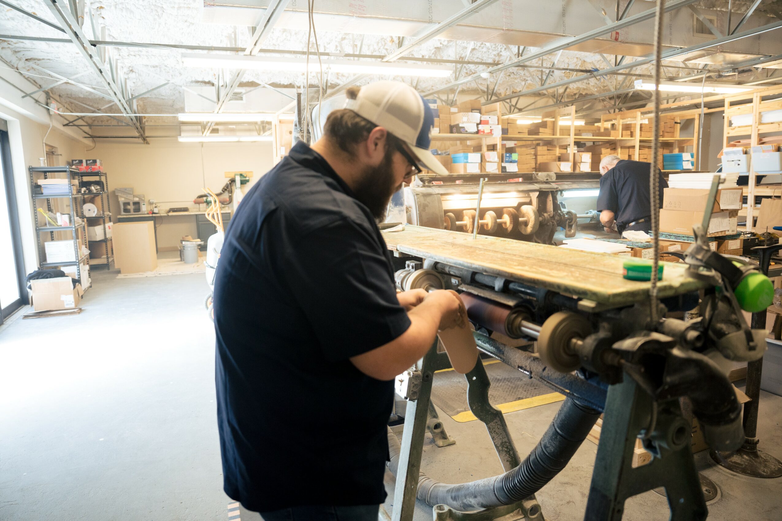 Person working with a tool in a workshop with shelves and equipment in the background.