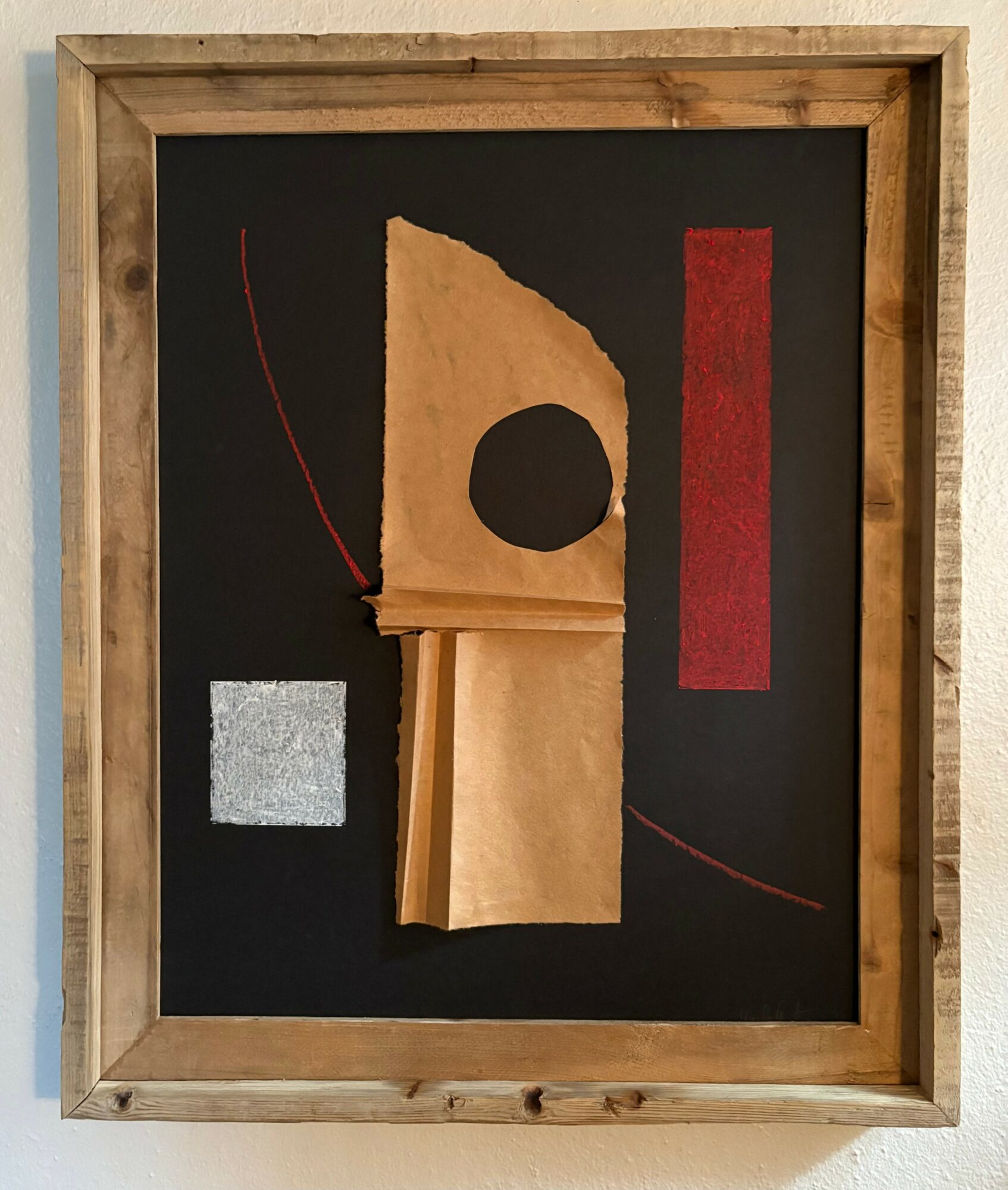 Abstract artwork with paper shapes, red and gray rectangles, and curved lines on a black background, framed in wood.