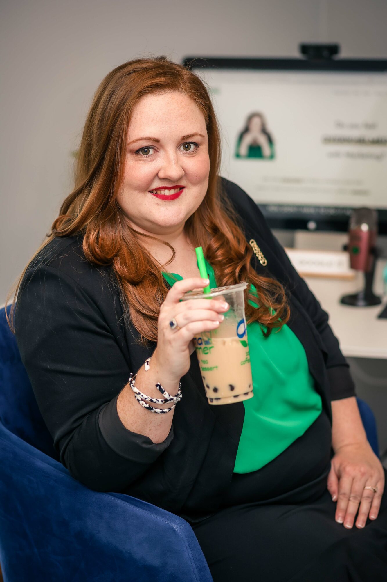 Woman with red hair and red lipstick holding a drink with a green straw, smiling at the camera.