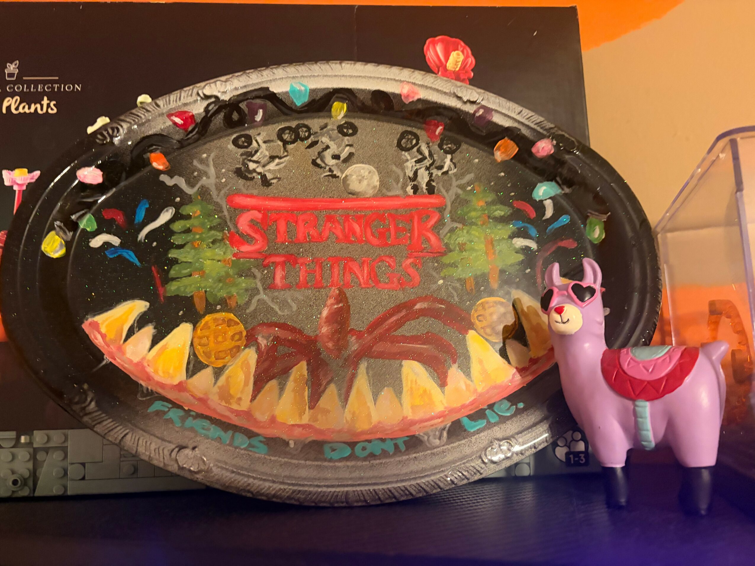 Stranger Things themed cake with a spider and colorful decorations, next to a pink and purple unicorn toy.
