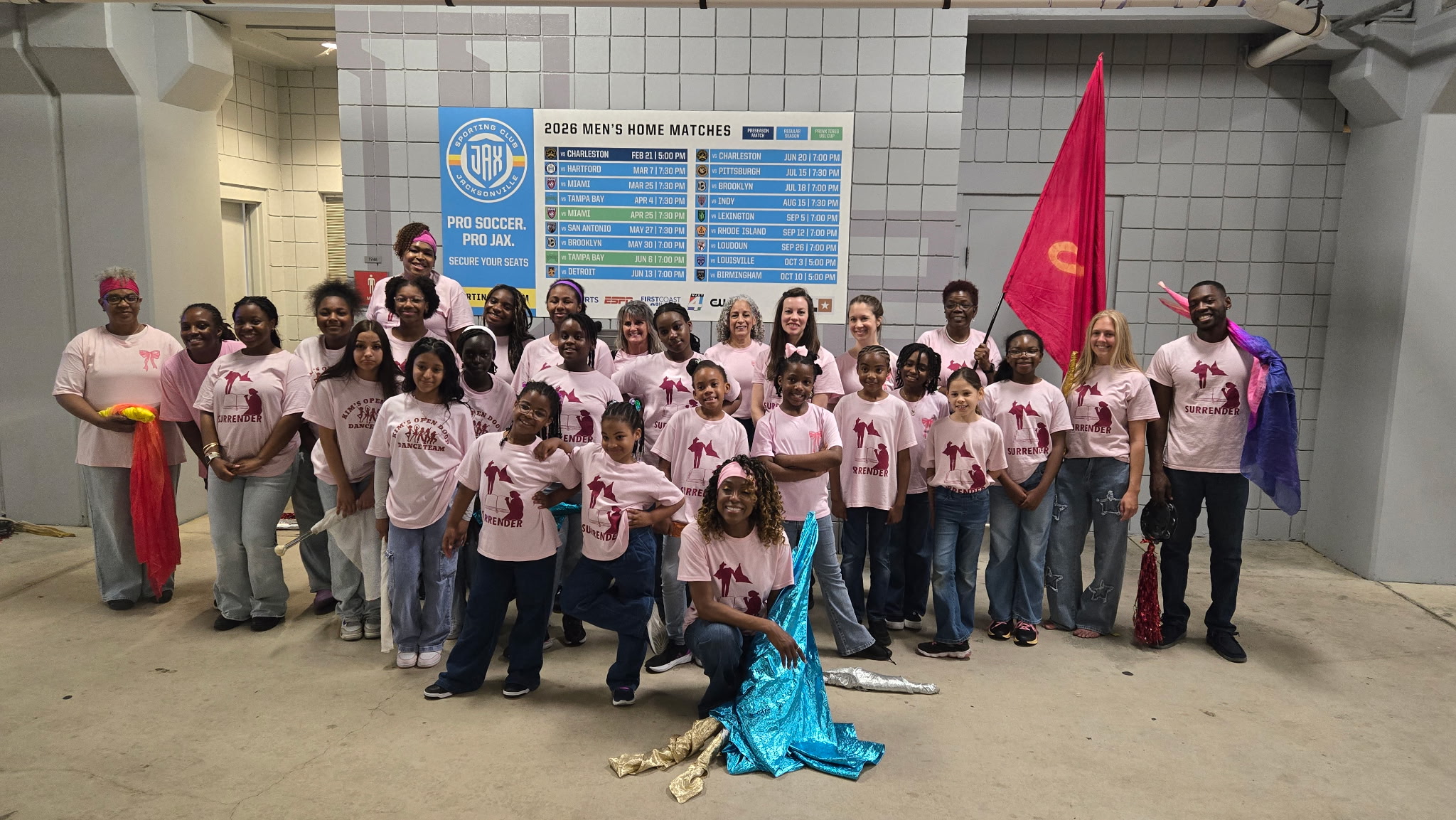 Group of people in pink shirts holding flags and banners, standing indoors in front of a blue sign, some holding flags.