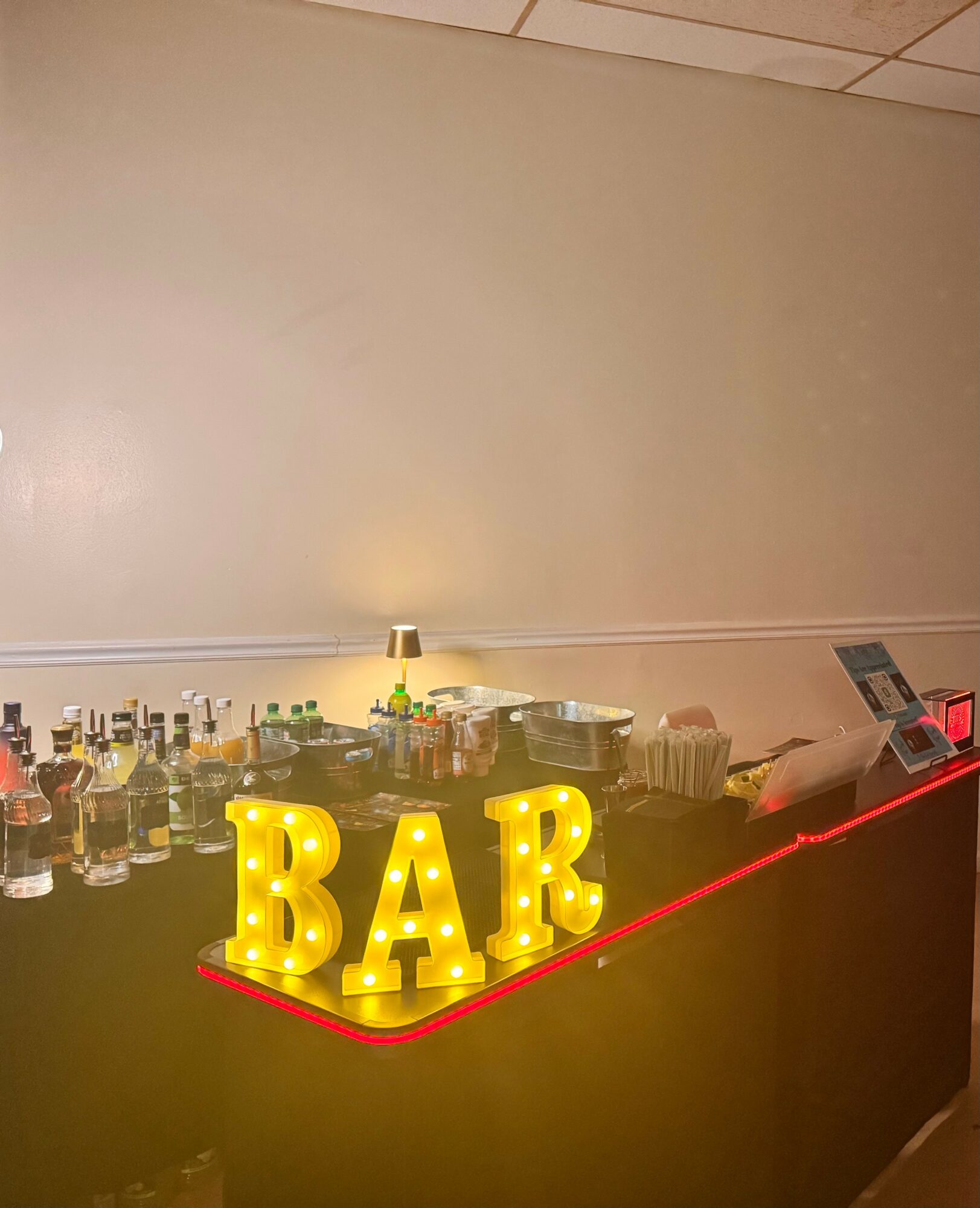 Bar counter with illuminated yellow letters spelling 'BAR' and various bottles behind it.