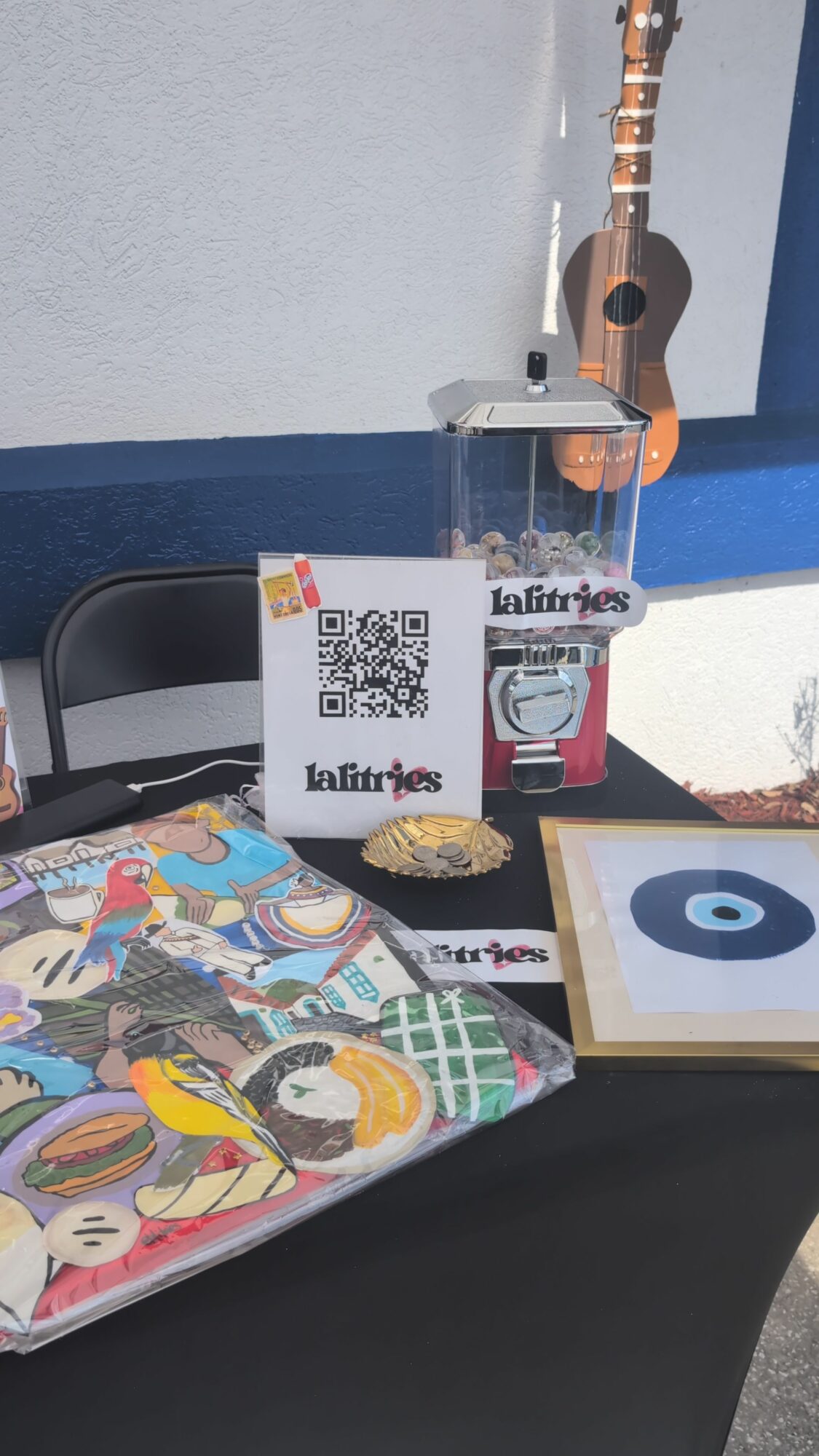 Table with a colorful puzzle, a framed eye artwork, a QR code sign, and a small container, against a white wall.