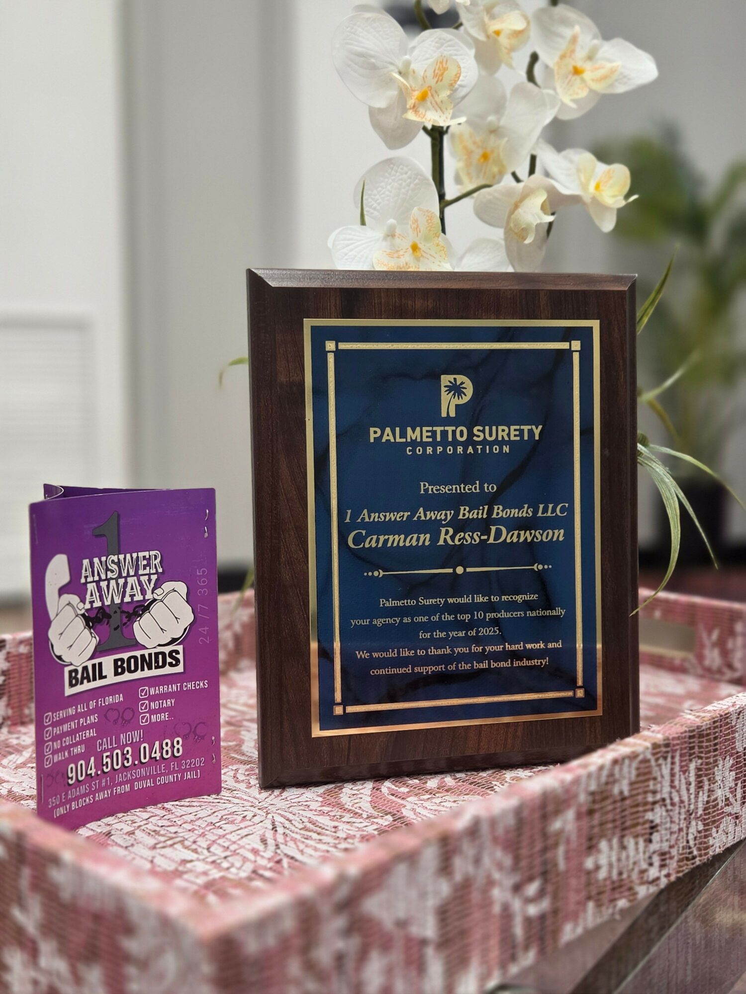 Award certificate in a wooden frame on a table with flowers and a pink tablecloth.