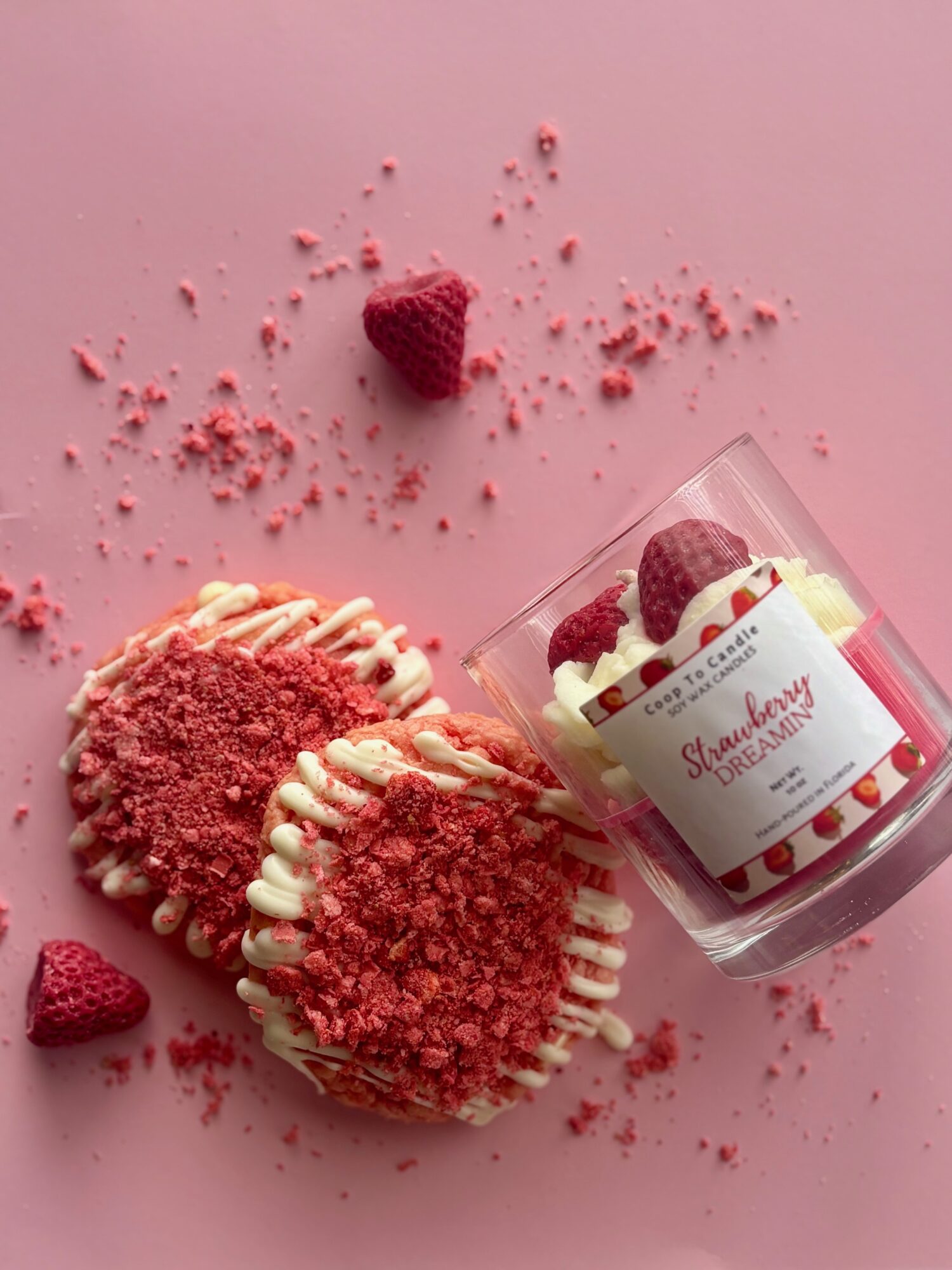Three strawberry-flavored desserts with crumb topping and white drizzle, a glass with strawberries and a label, on pink background.
