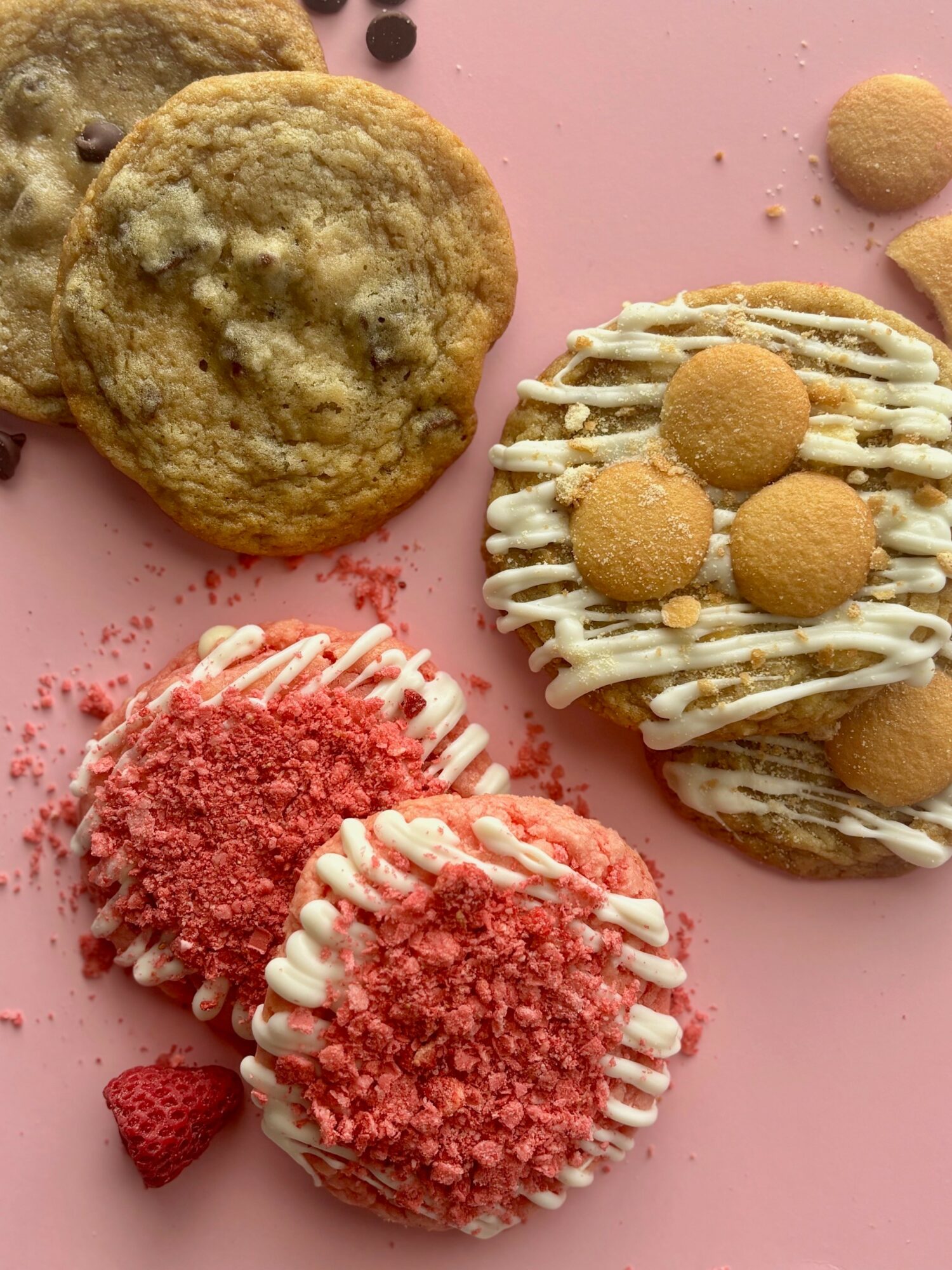 Cookies and decorated cupcakes on a pink surface, some with pink crumbs and white icing, others with cookies and drizzle.