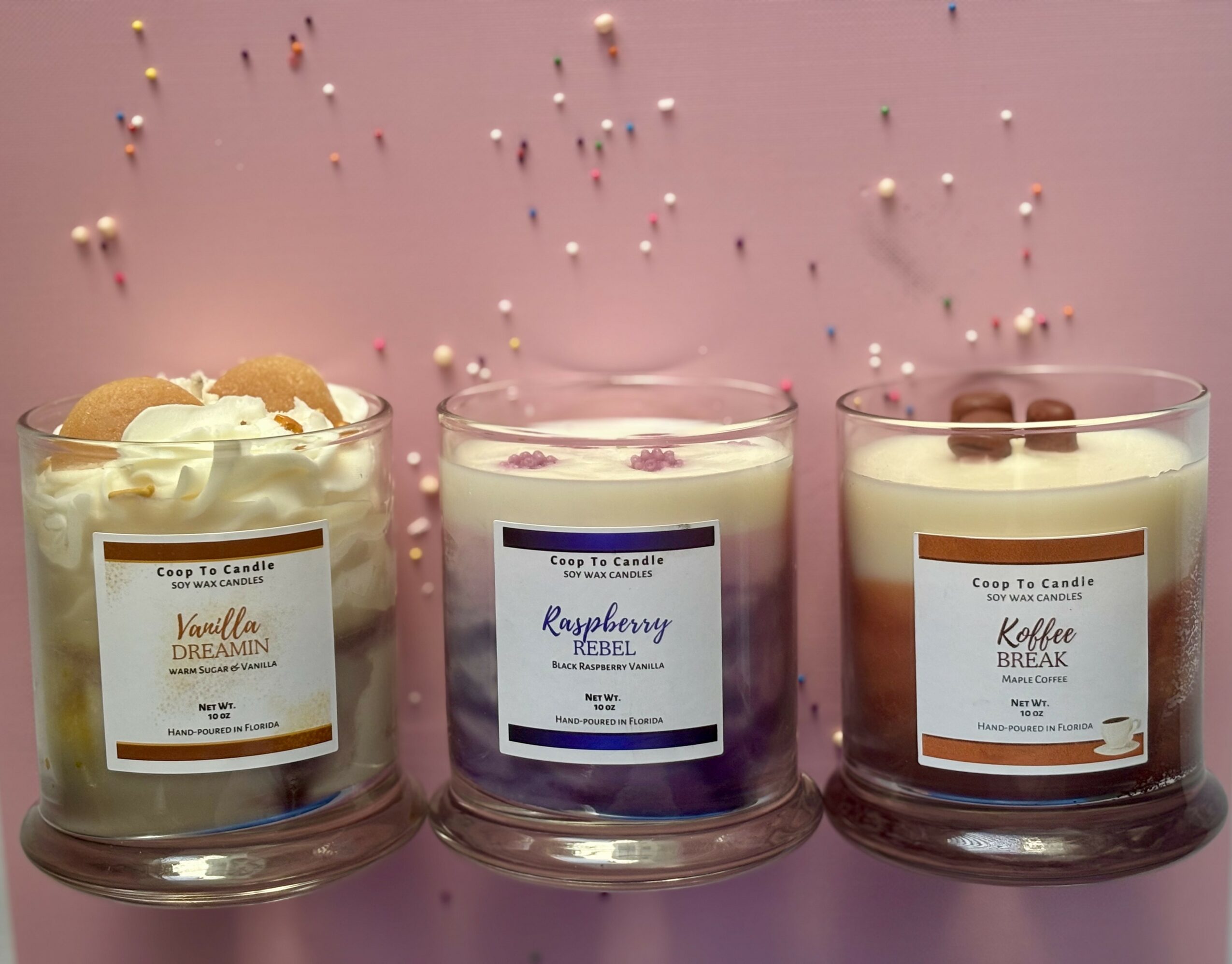 Three candles with labels, one with whipped cream and cookies, on a pink surface with scattered beads.