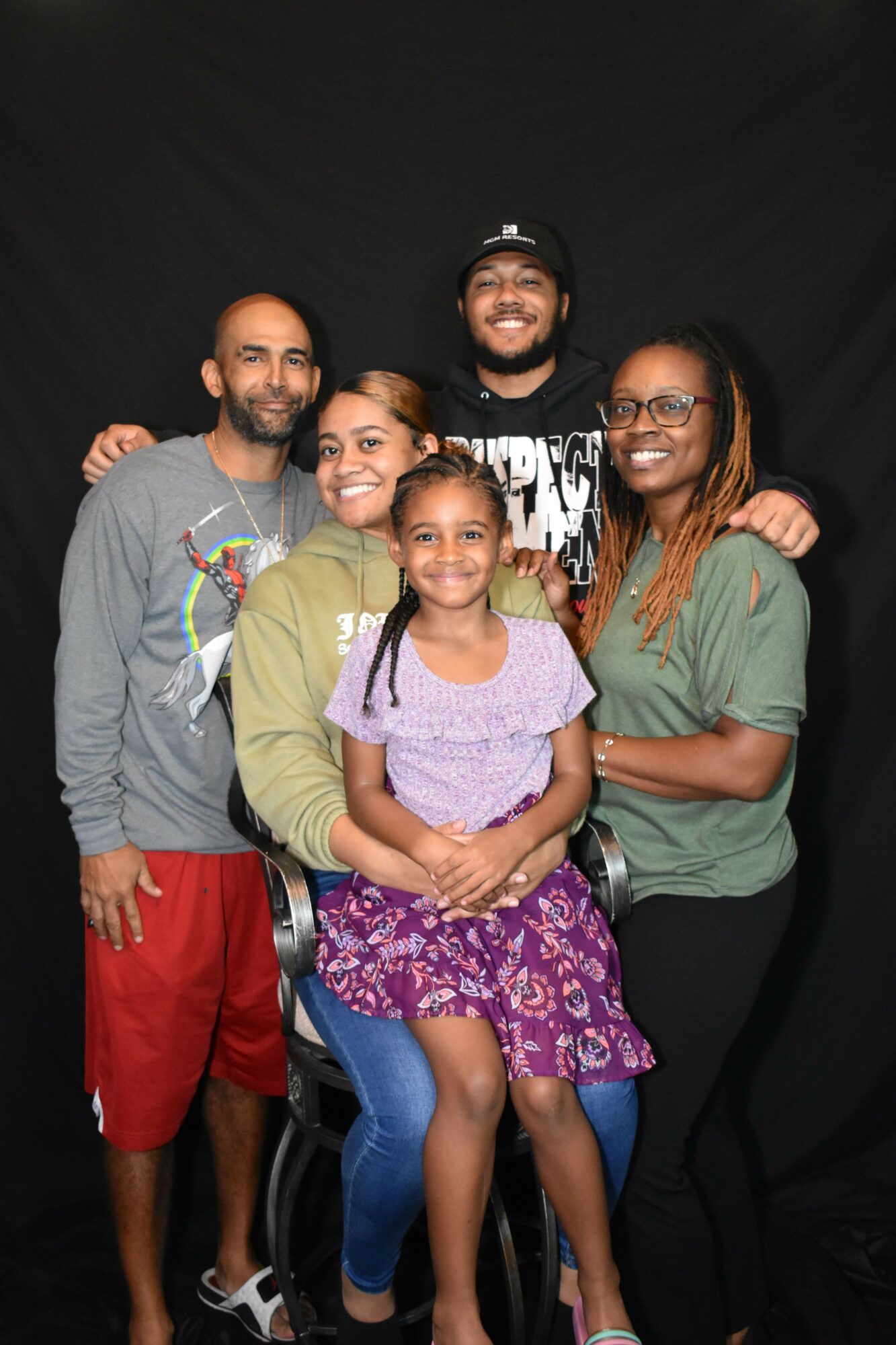 Group of five people, including children and adults, smiling and posing together against a black background.