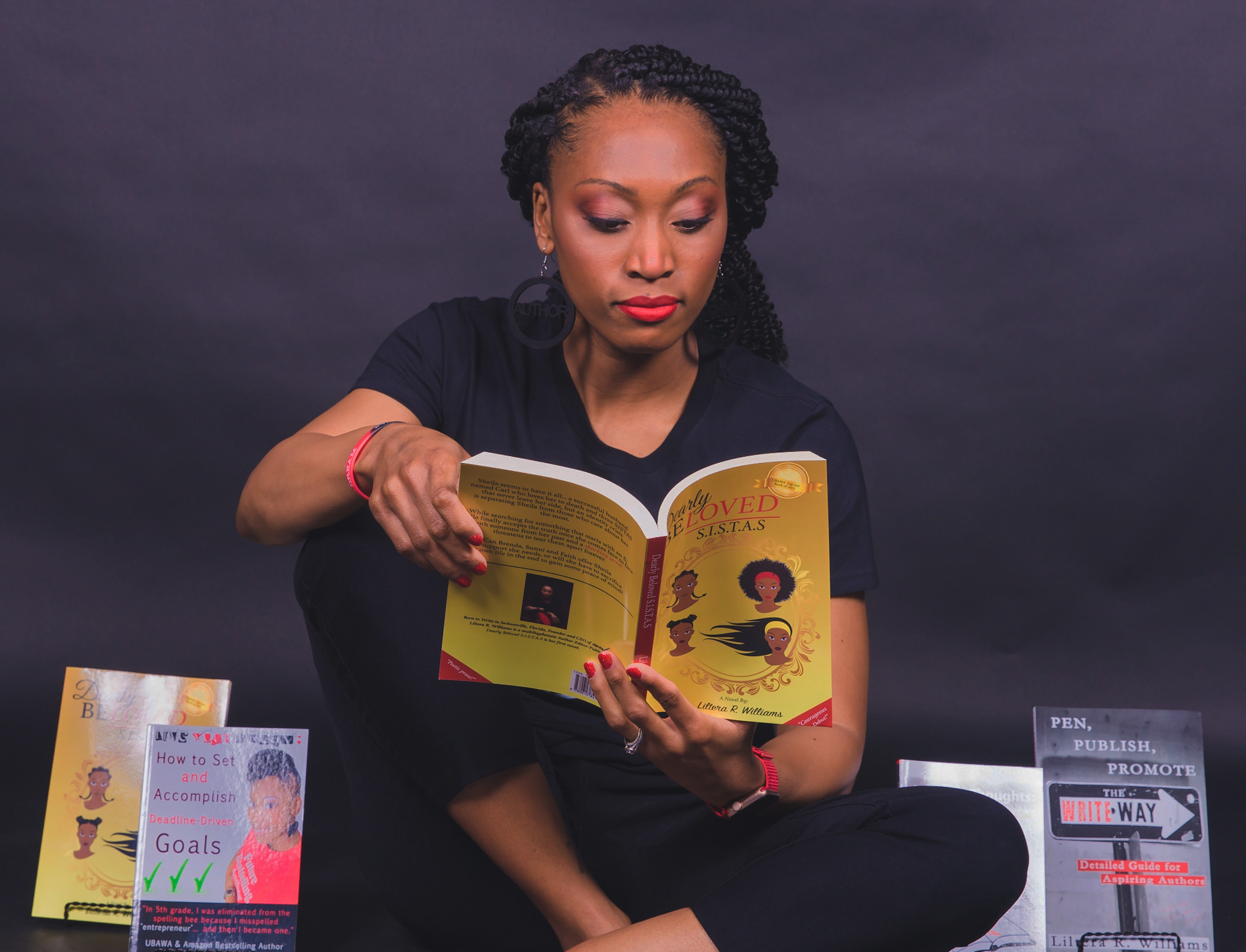 Woman sitting cross-legged reading a book, with pamphlets on either side, against a dark background.