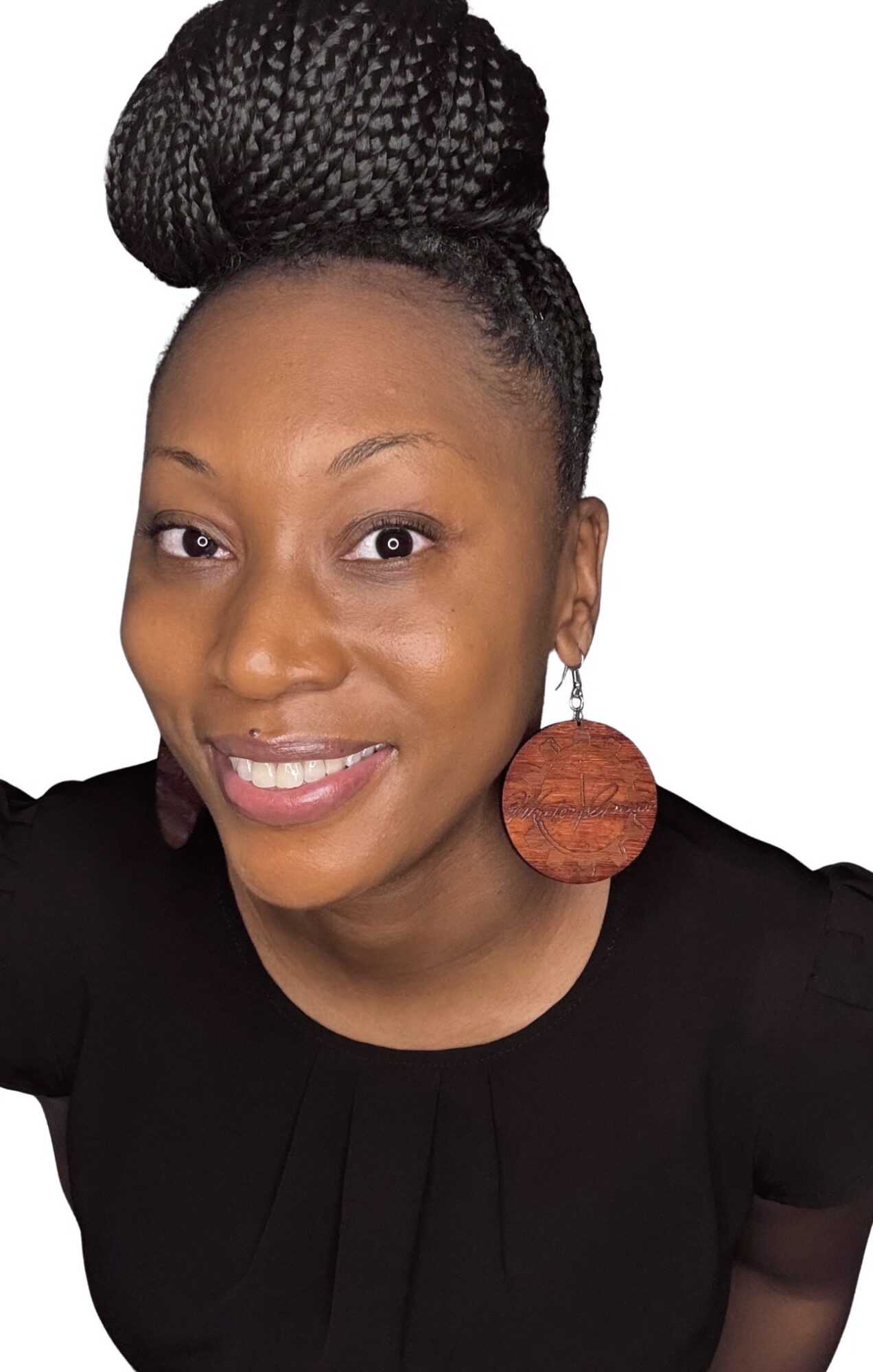 Woman with braided hair styled in a high bun, wearing large round earrings and a black top, smiling.