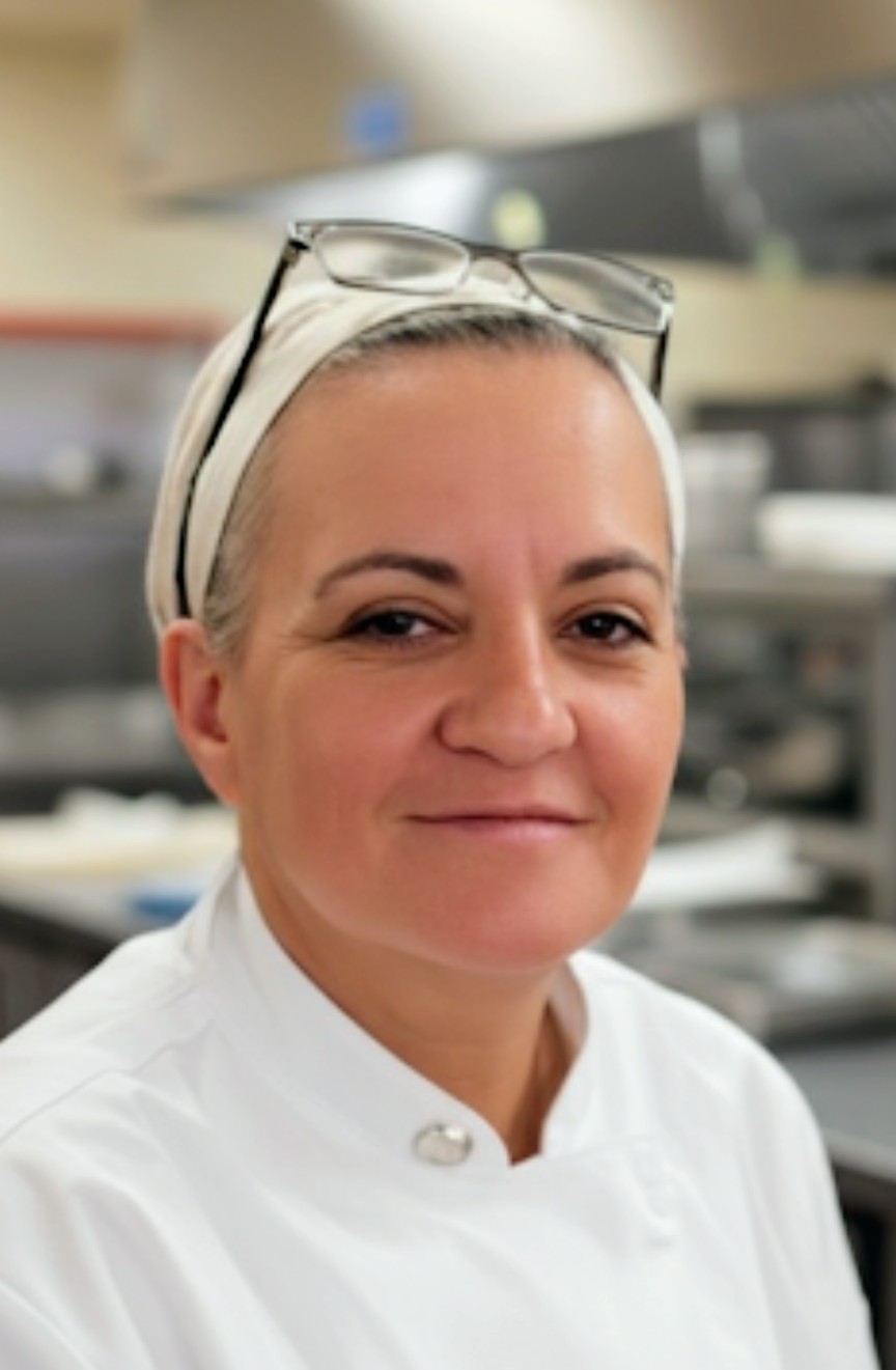 Woman with glasses on head wearing a white uniform in a professional kitchen or laboratory setting.