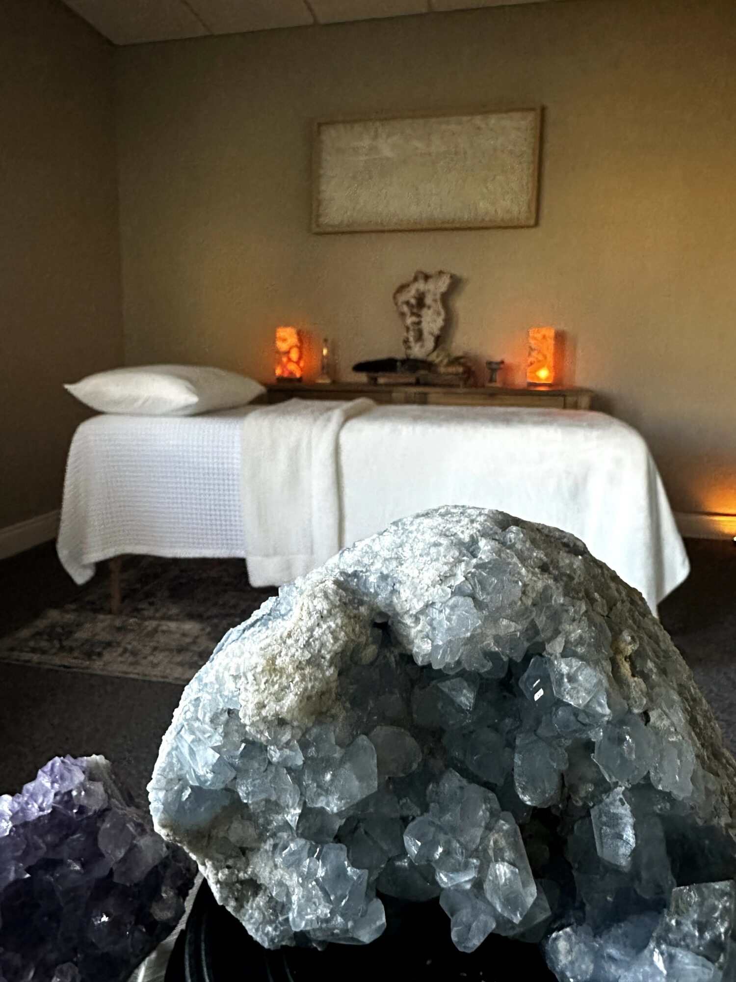 A room with a bed, decorative objects, and a large crystal in the foreground, with a framed artwork on the wall.