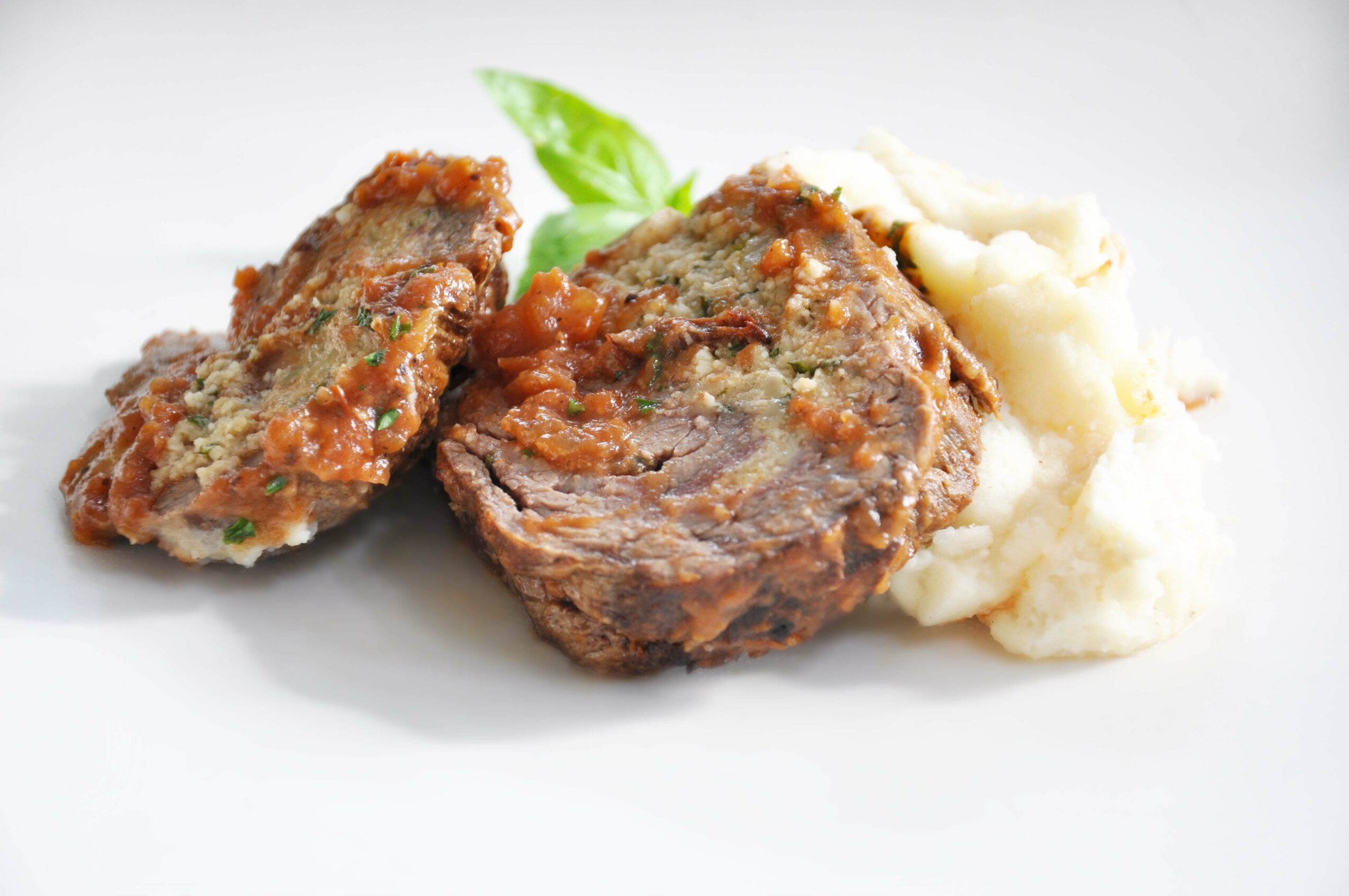 Two cooked meatloaf slices with mashed potatoes and a green garnish on a white plate.