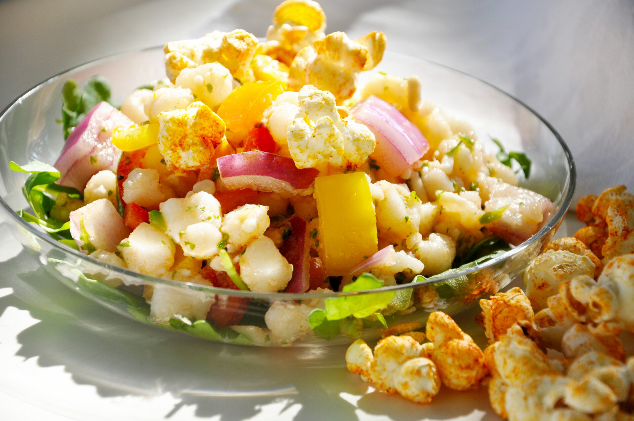 Salad with corn, onions, and cheese in a glass bowl, with popcorn on the side