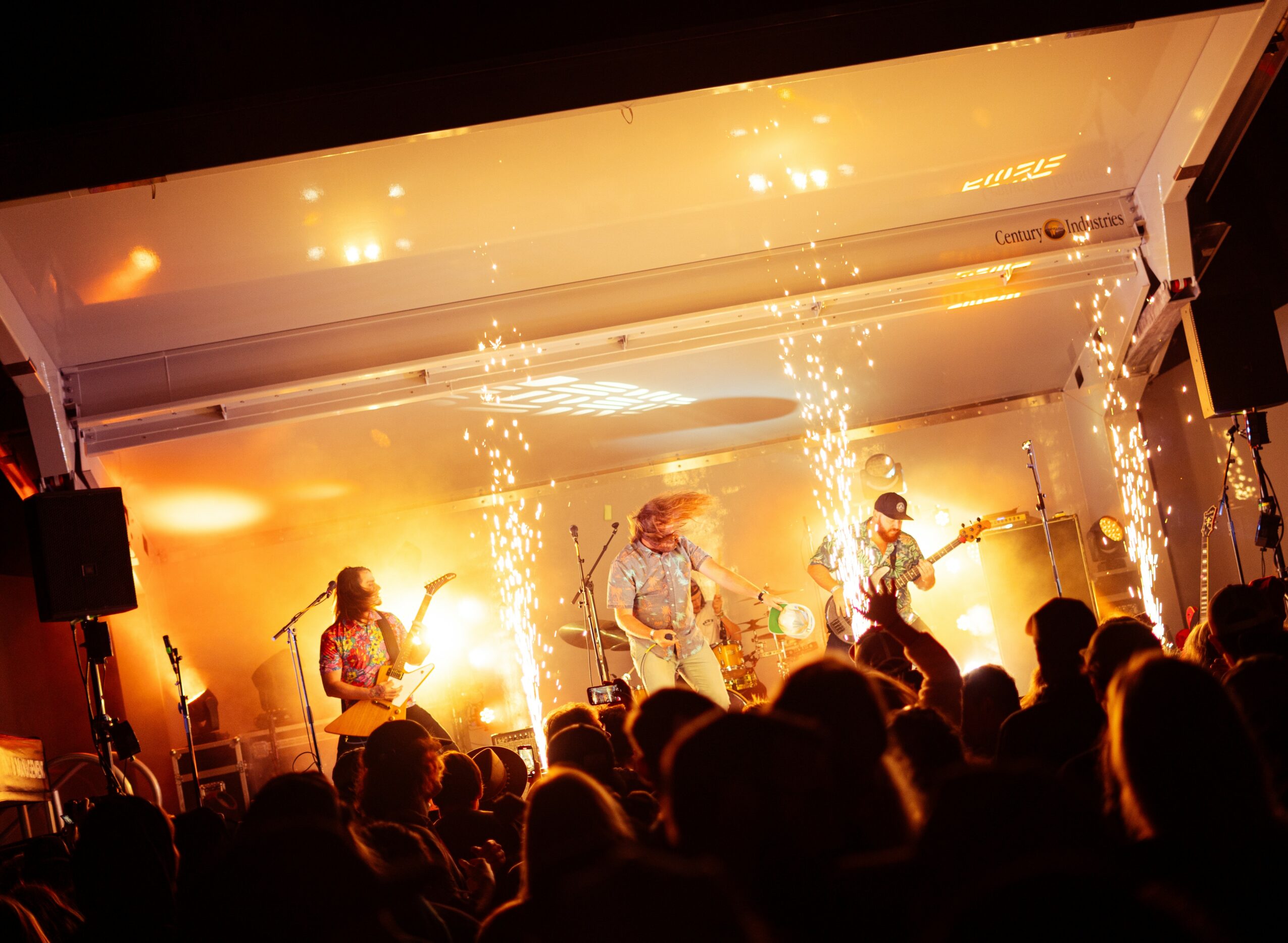 Band performs on stage with bright lights and sparks, audience watching attentively, indoor concert setting.