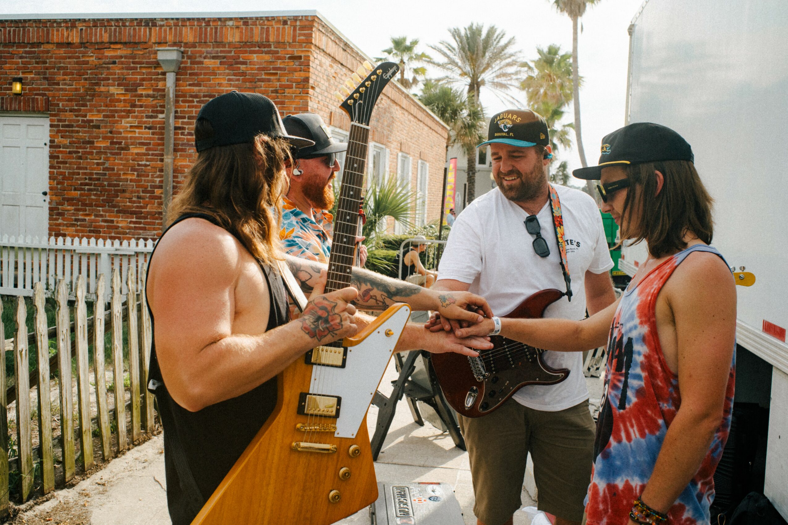 Four people outdoors, two women and two men, engaged in conversation, with musical instruments and a white van in background.