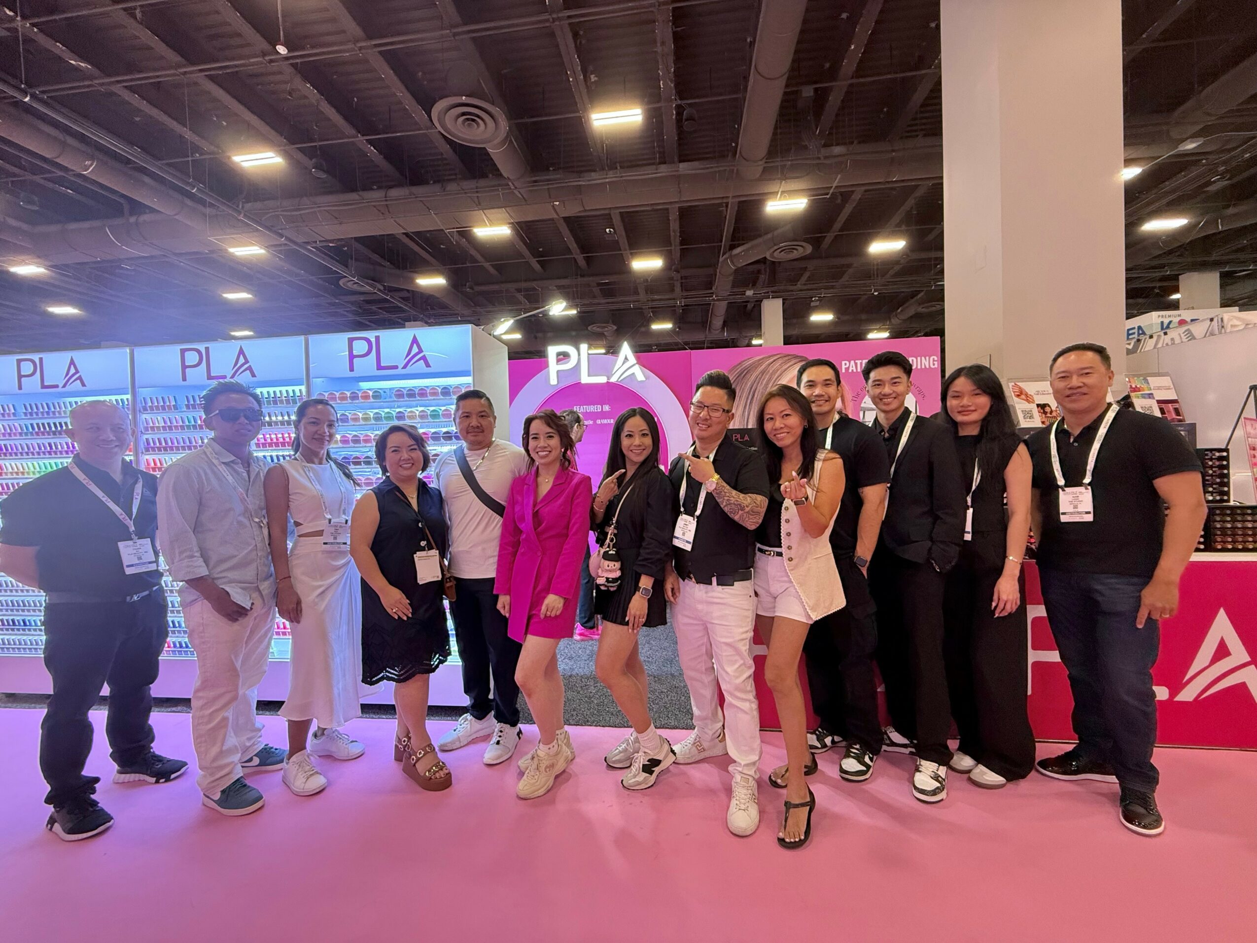 Group of people standing together at an indoor event with screens displaying 'PLA' in the background.