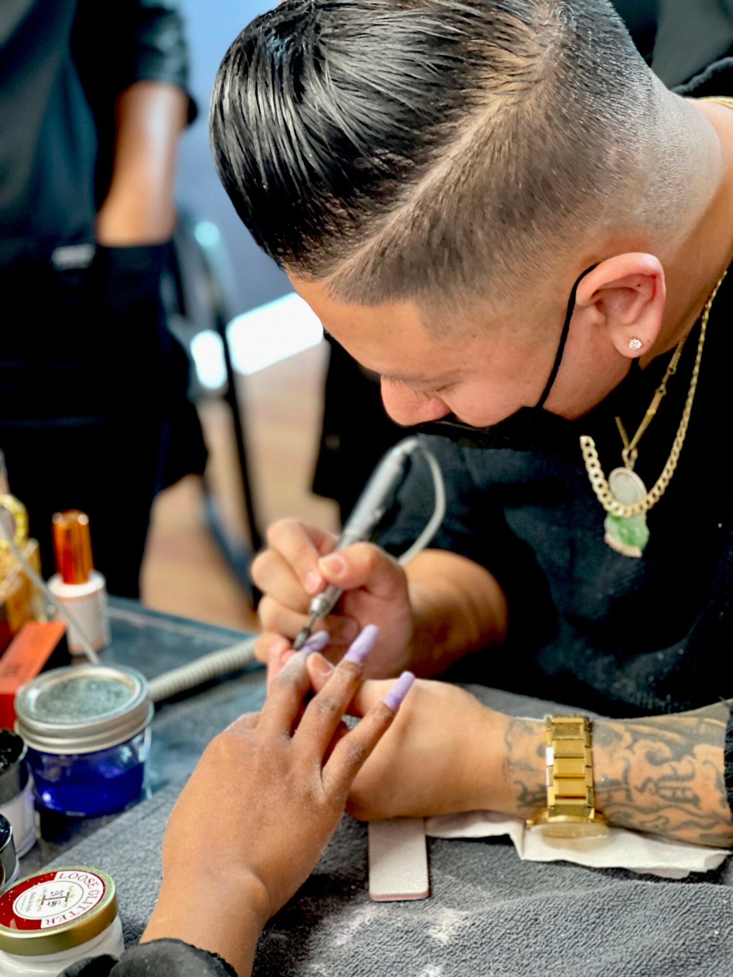 Person getting a nail manicure, with tools and nail polish on table, focusing on hand and nails.