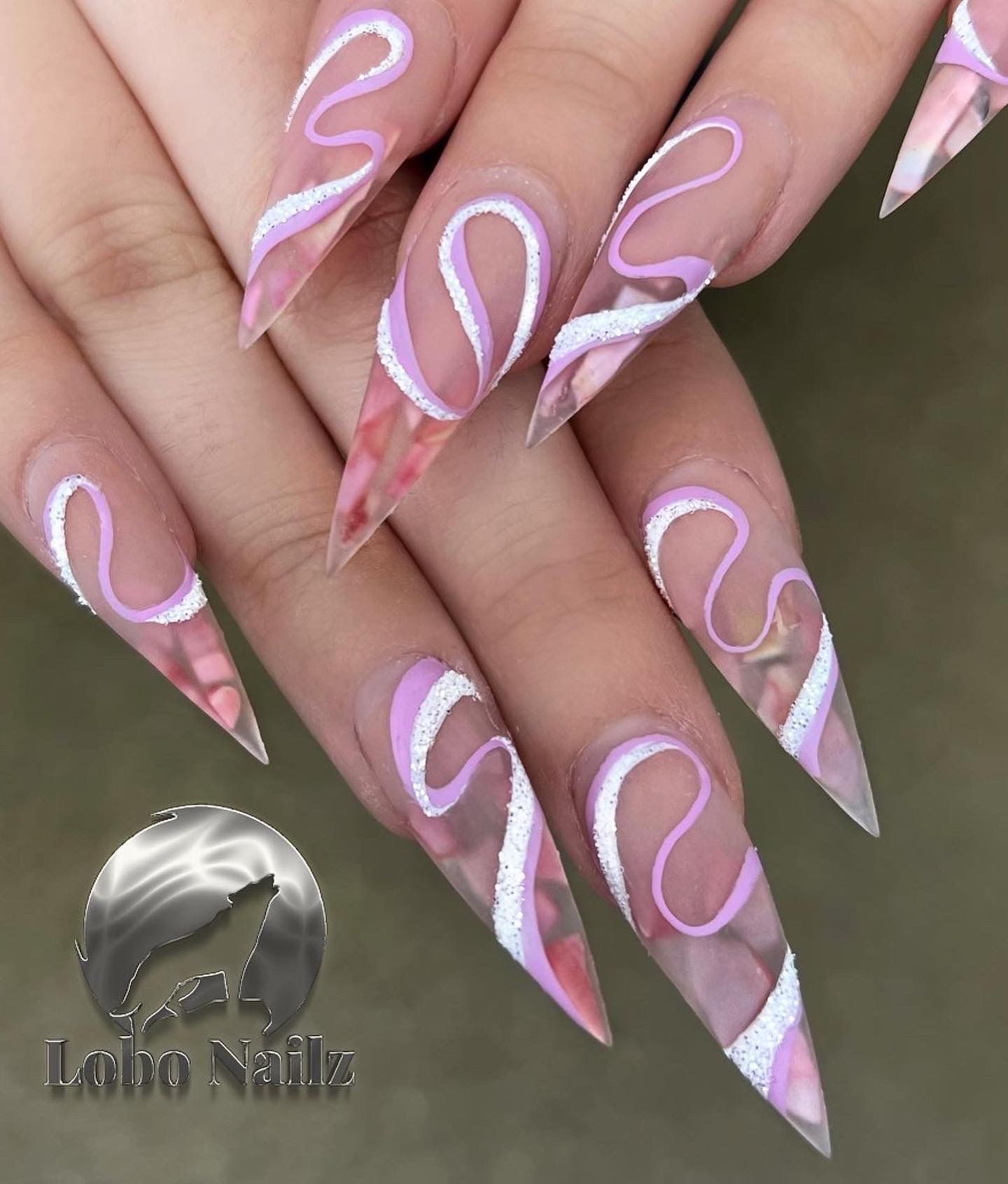 Close-up of long, pointed nails with pink and white swirling designs, held together with fingers visible.
