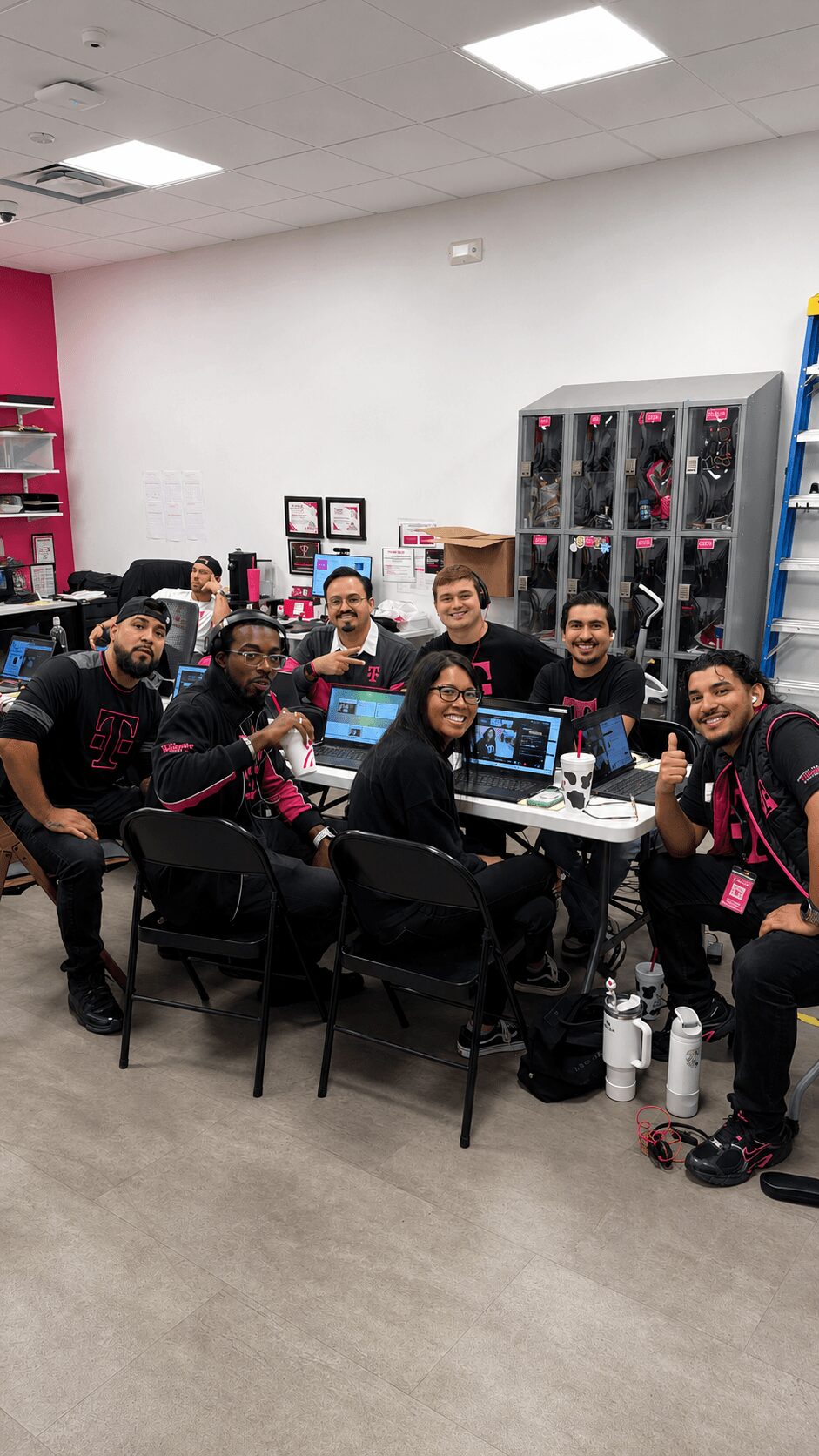 Group of nine people sitting around a table in a room with pink and white walls, smiling at the camera.