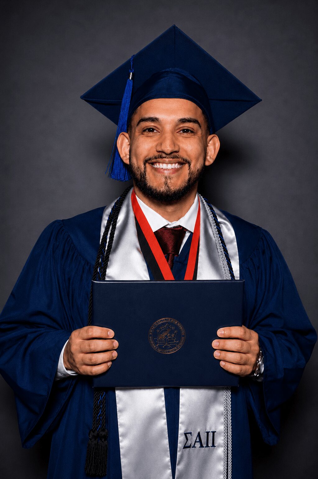 Graduate in cap and gown holding diploma, smiling, against dark background.