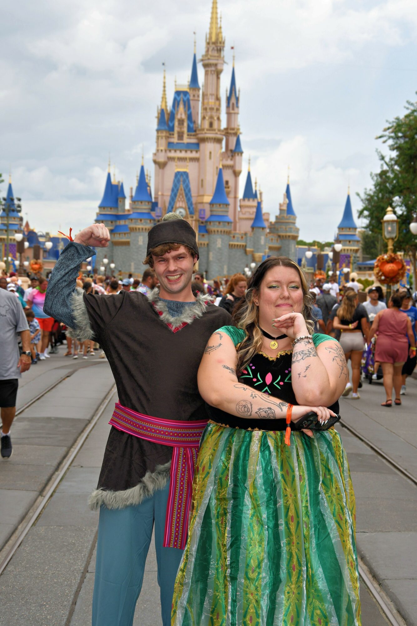 Two people stand in front of a castle at a theme park, smiling and posing for the photo.