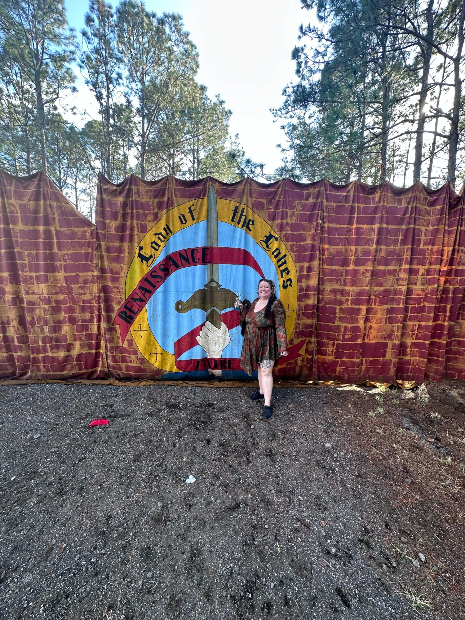 Person standing in front of a colorful banner with a crossed-out dog symbol, outdoors with trees in the background.