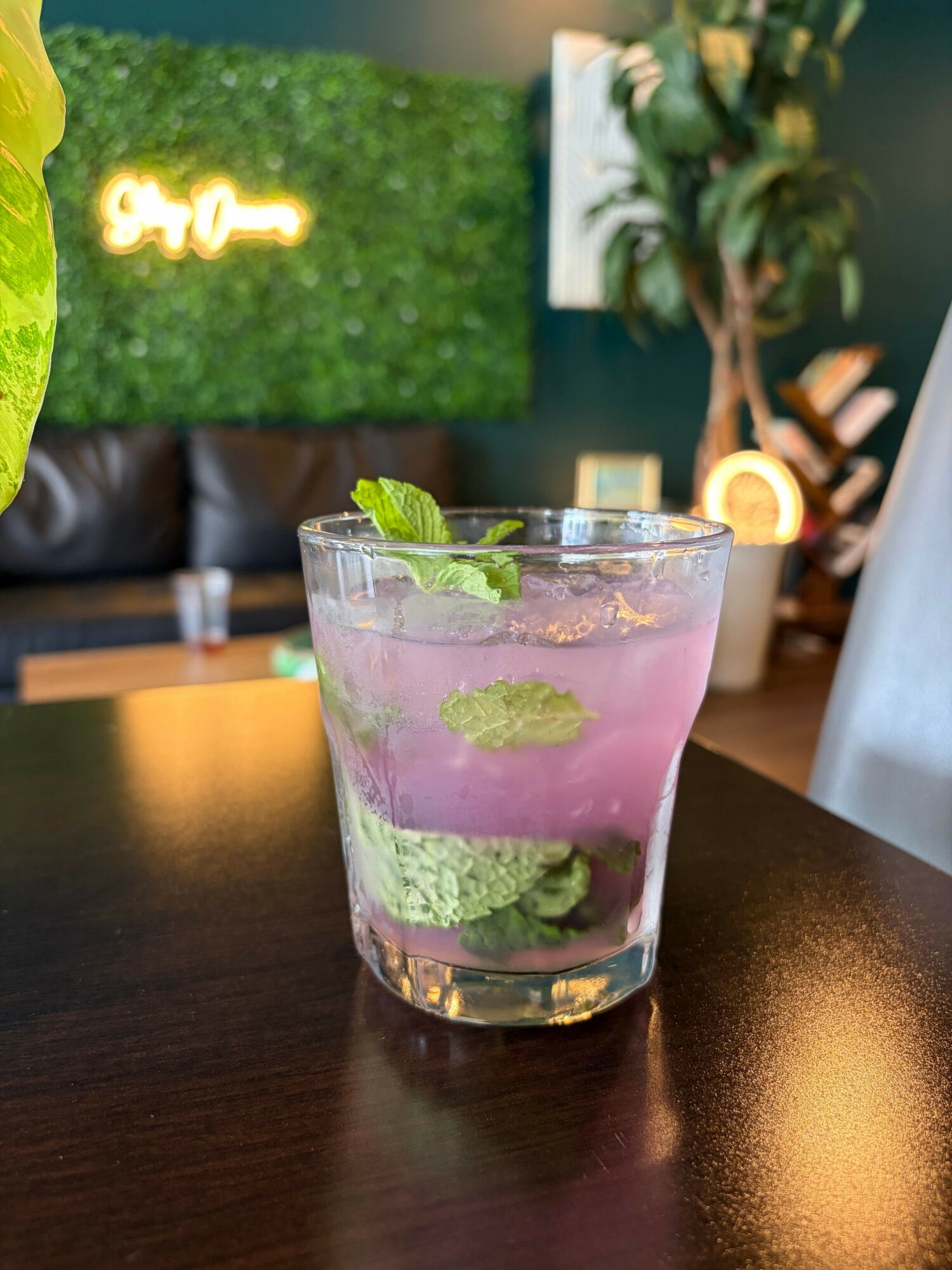 A glass of pink and green layered drink on a dark table with a blurred background.