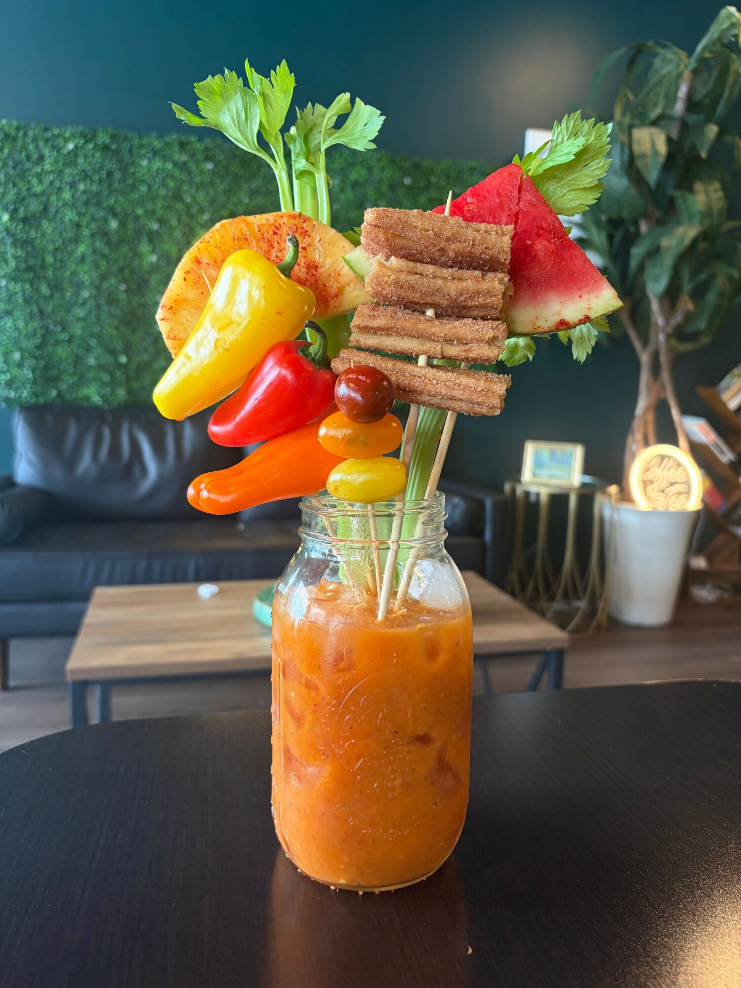 A colorful vegetable and fruit arrangement with a drink in a glass jar, on a dark table in a cozy setting.