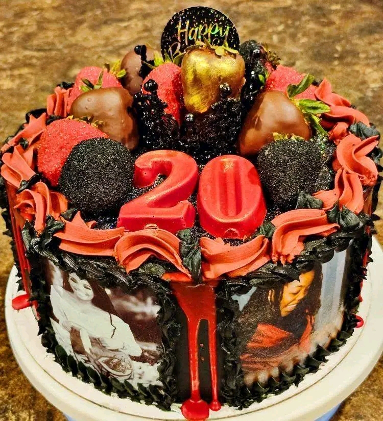 Round birthday cake decorated with strawberries, chocolates, black candies, red frosting, and a 'Happy' topper, celebrating 20 years.