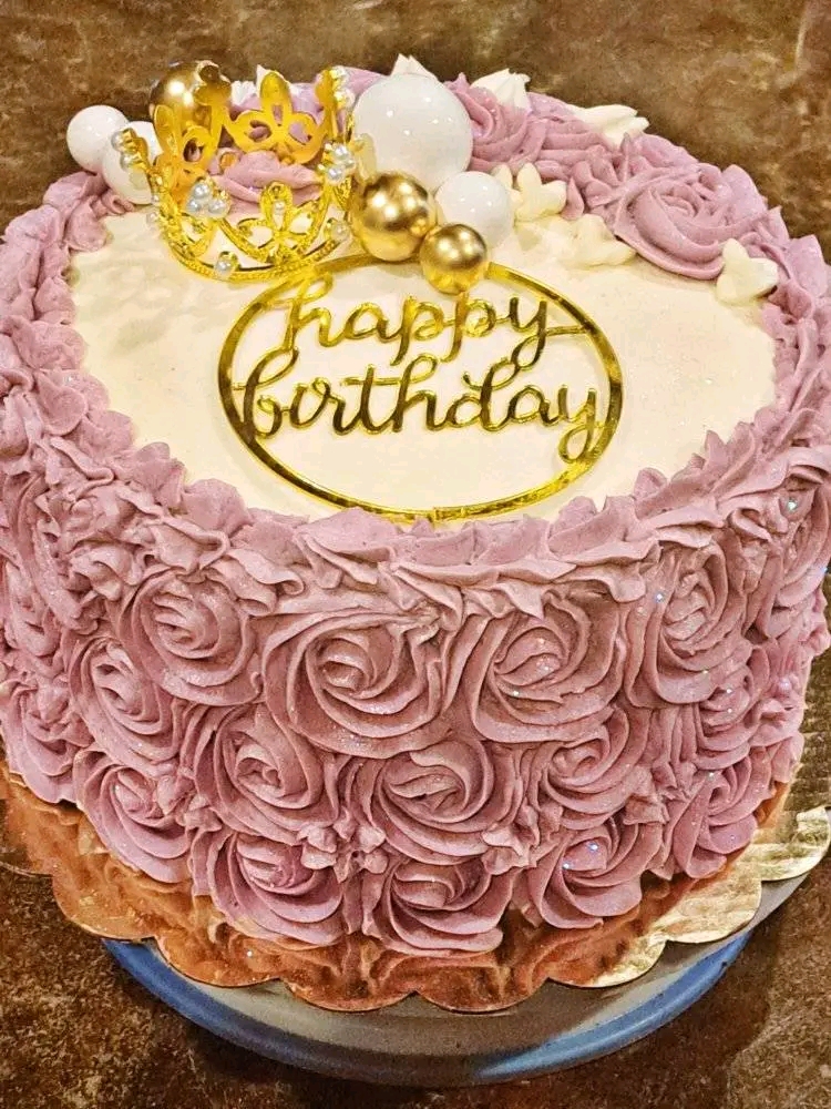 Round birthday cake decorated with pink rosette frosting, a gold 'happy birthday' topper, and small decorative elements on top.