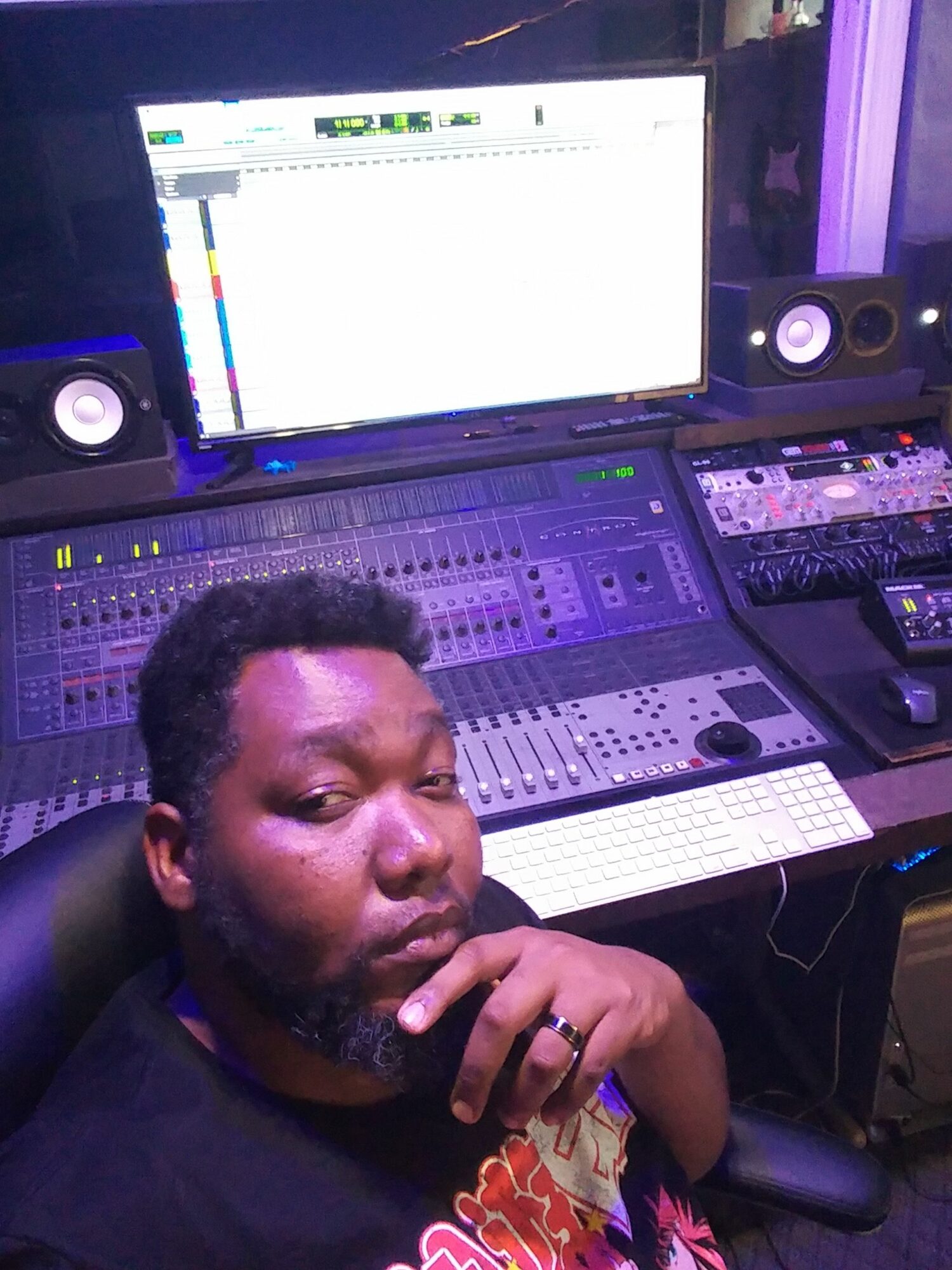 Person with hand on chin in a music studio with computer monitors and audio equipment.
