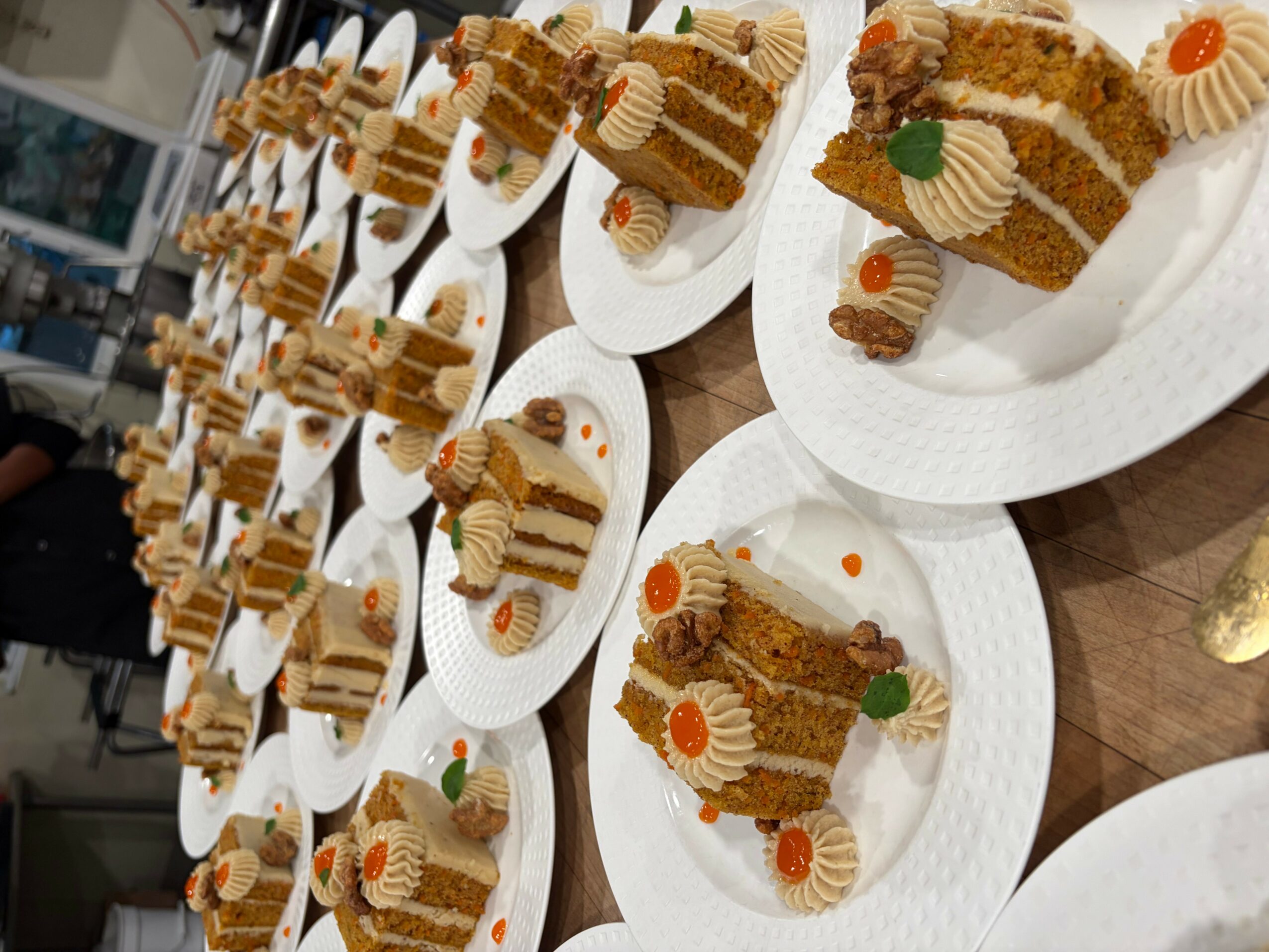 Multiple plates with layered cake slices, decorated with cream, orange dots, and small green leaves, arranged on a table.