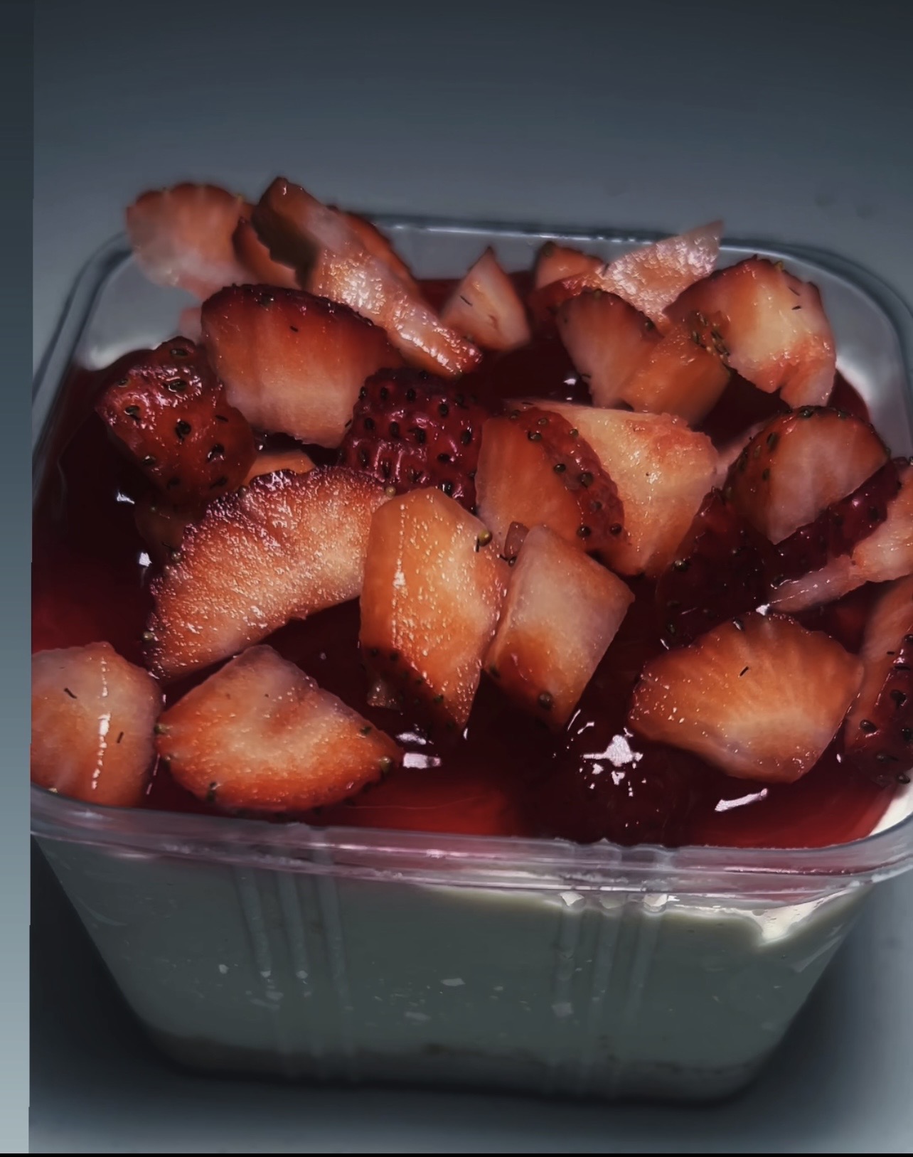 Glass container filled with chopped strawberries and a red syrup or sauce, on a dark surface.