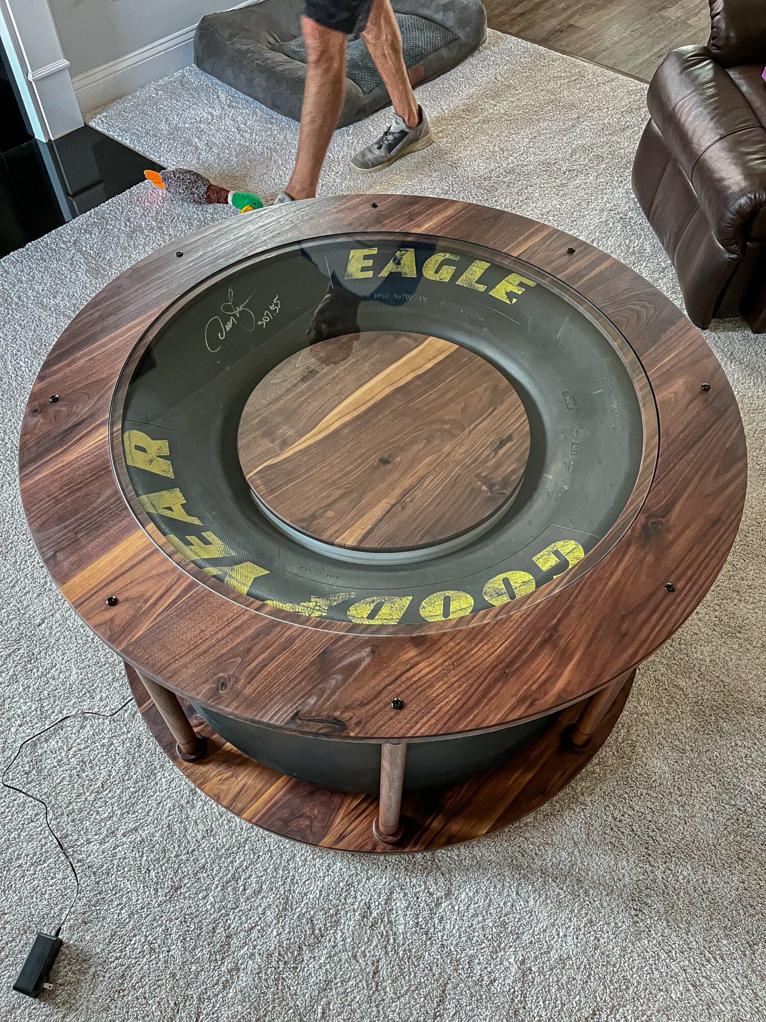 Round wooden table with a glass top displaying yellow and black text, situated on a carpeted floor in a room.