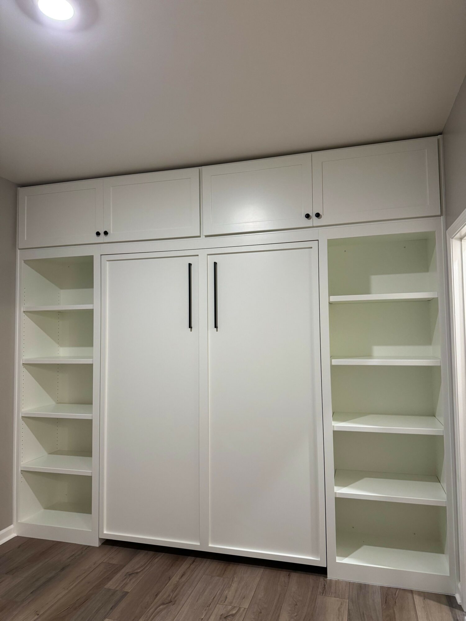 White storage cabinet with glass doors and open shelves, against a light-colored wall, on a wooden floor.