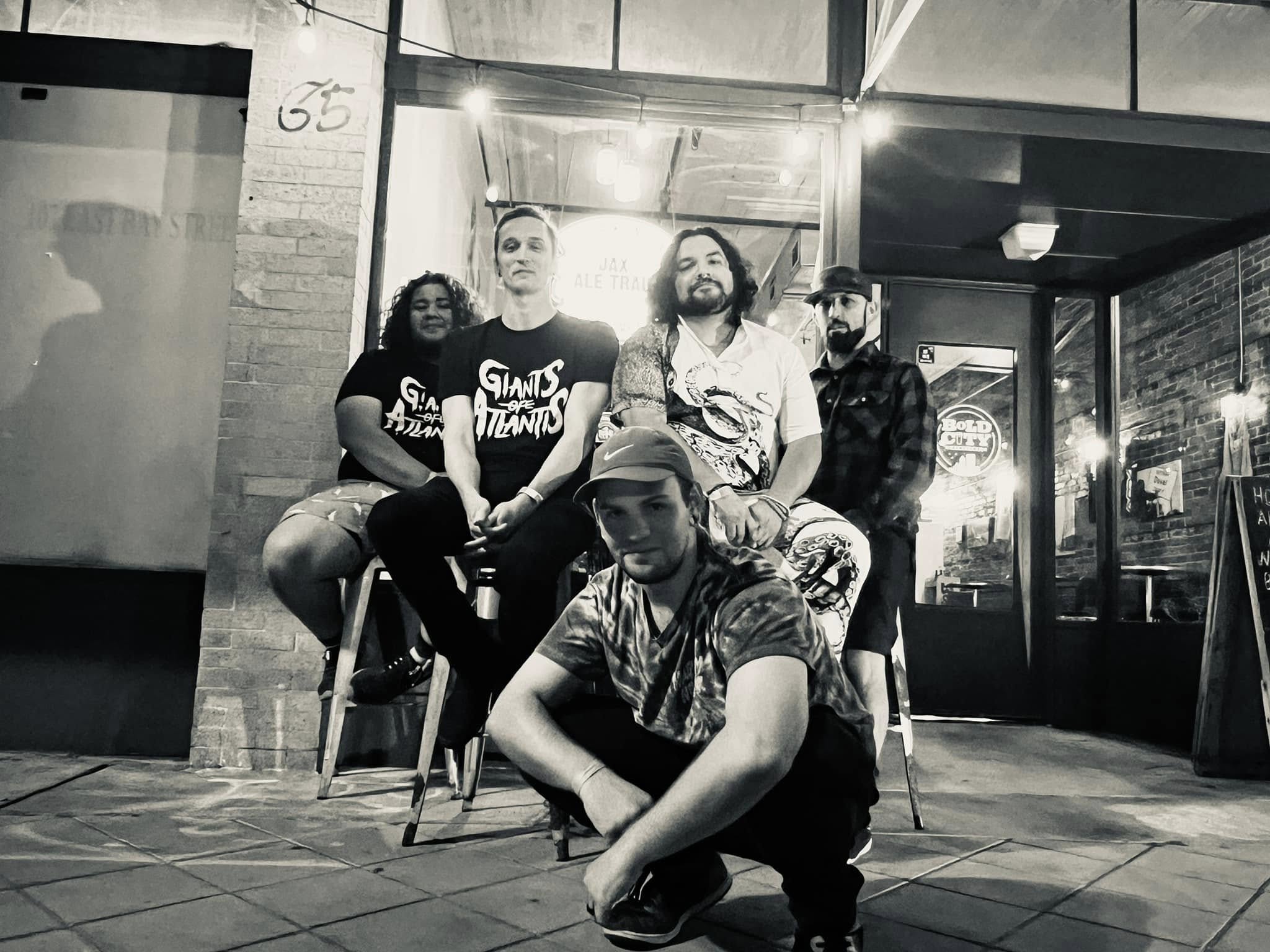 Group of six people sitting and standing outside a building at night, some smiling, in black and white.