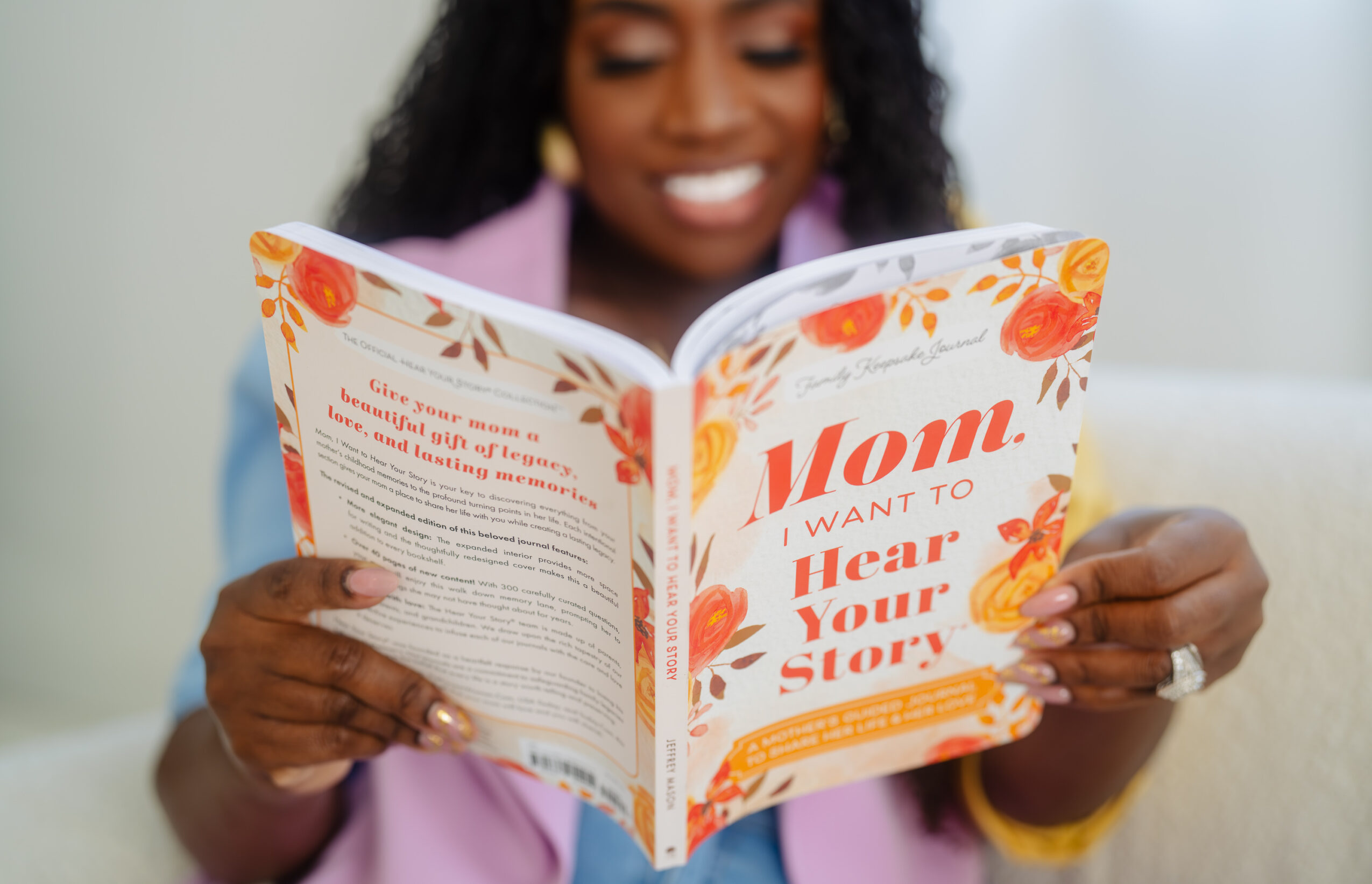 Person reading a colorful book with orange and yellow floral designs, smiling, indoors.