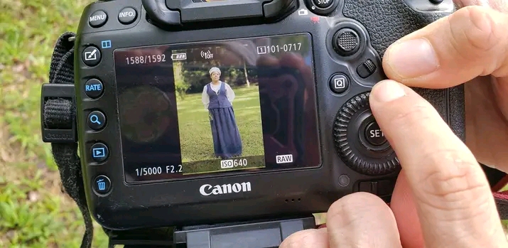 Camera screen shows a person standing outdoors with trees in the background.